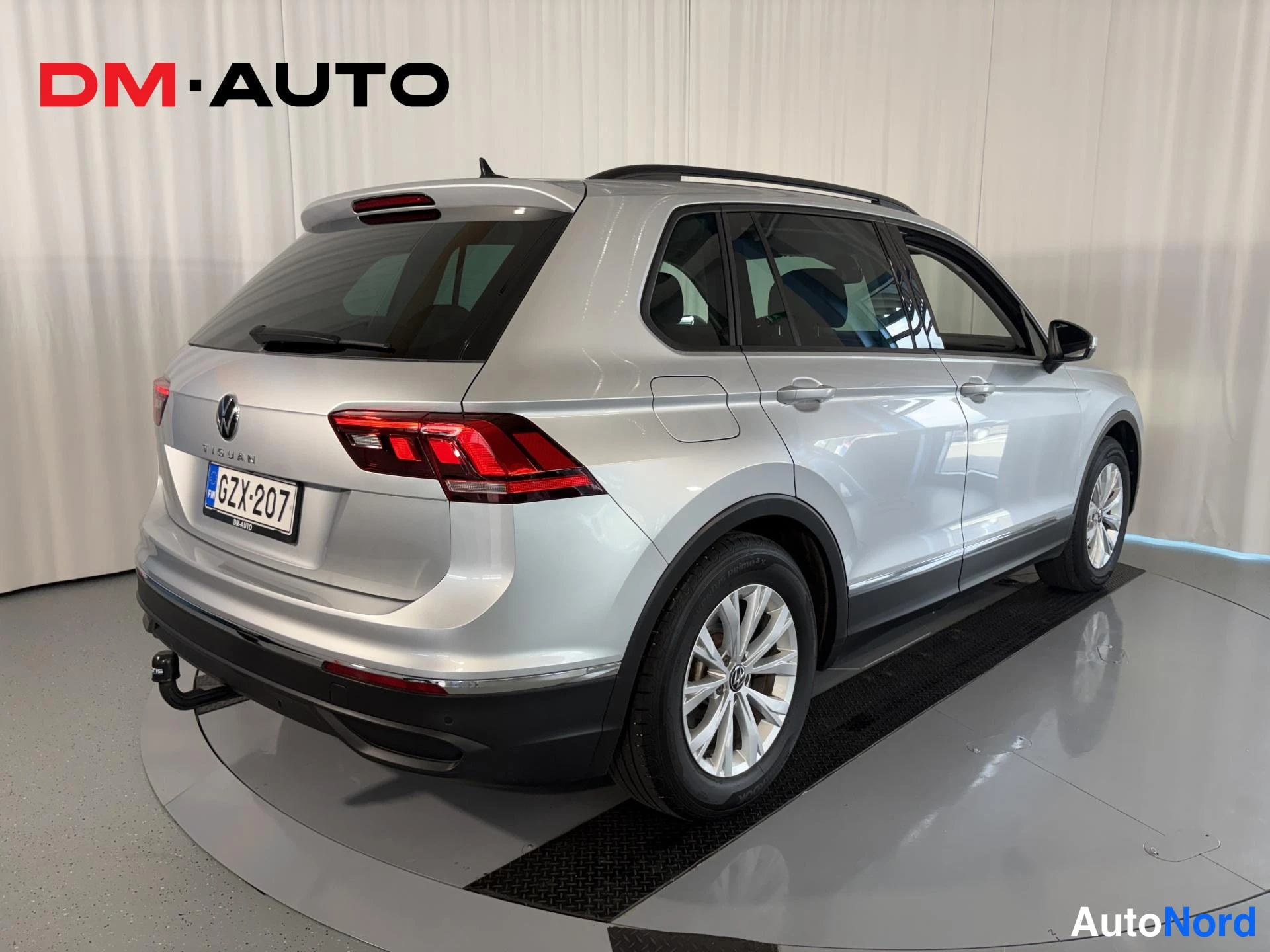 Takaviisto: Hopeanvärinen Volkswagen Tiguan takaa vasemmalta kuvattuna; rekisteritunnus, vetokoukku ja kattokaiteet näkyvät.