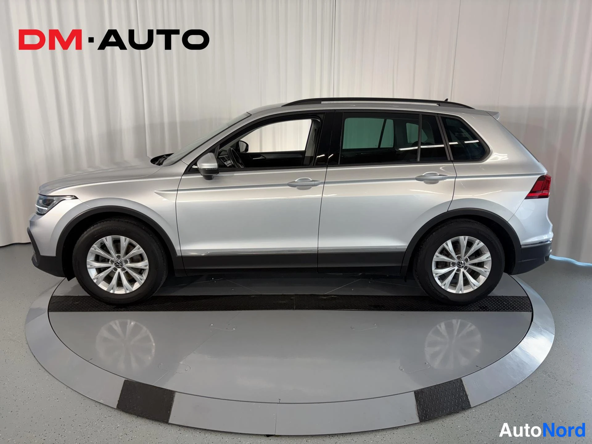 Sivulta: Hopeanvärinen Volkswagen Tiguan sivulta vasemmalta; kattokaiteet ja hopeavanteet näkyvät.