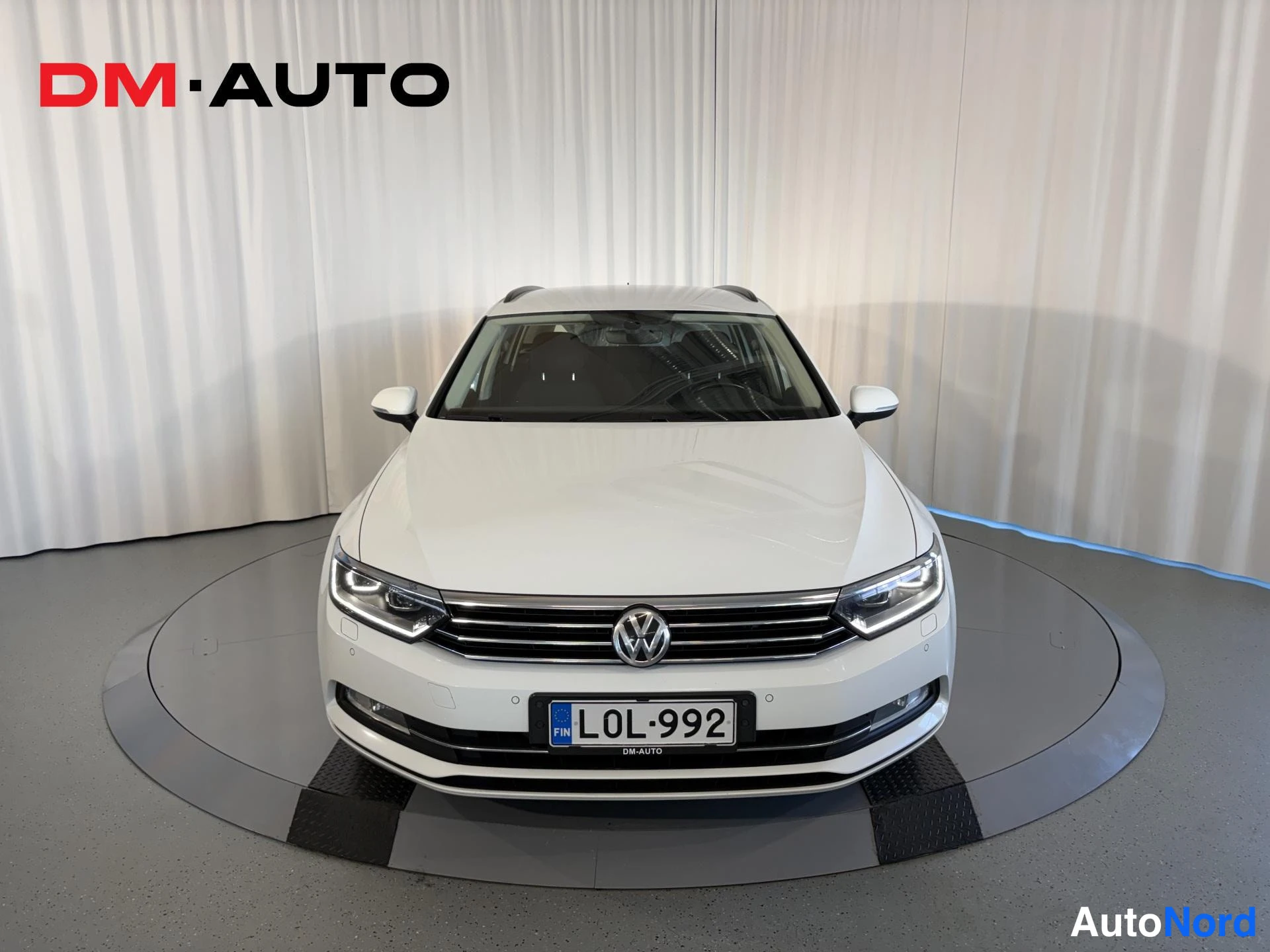Edestä: Valkoinen Volkswagen Passat Variant suoraan edestä kuvattuna, LE-divaani, rekisterikilpi, etukorin ja ajovalot näkyvät.
