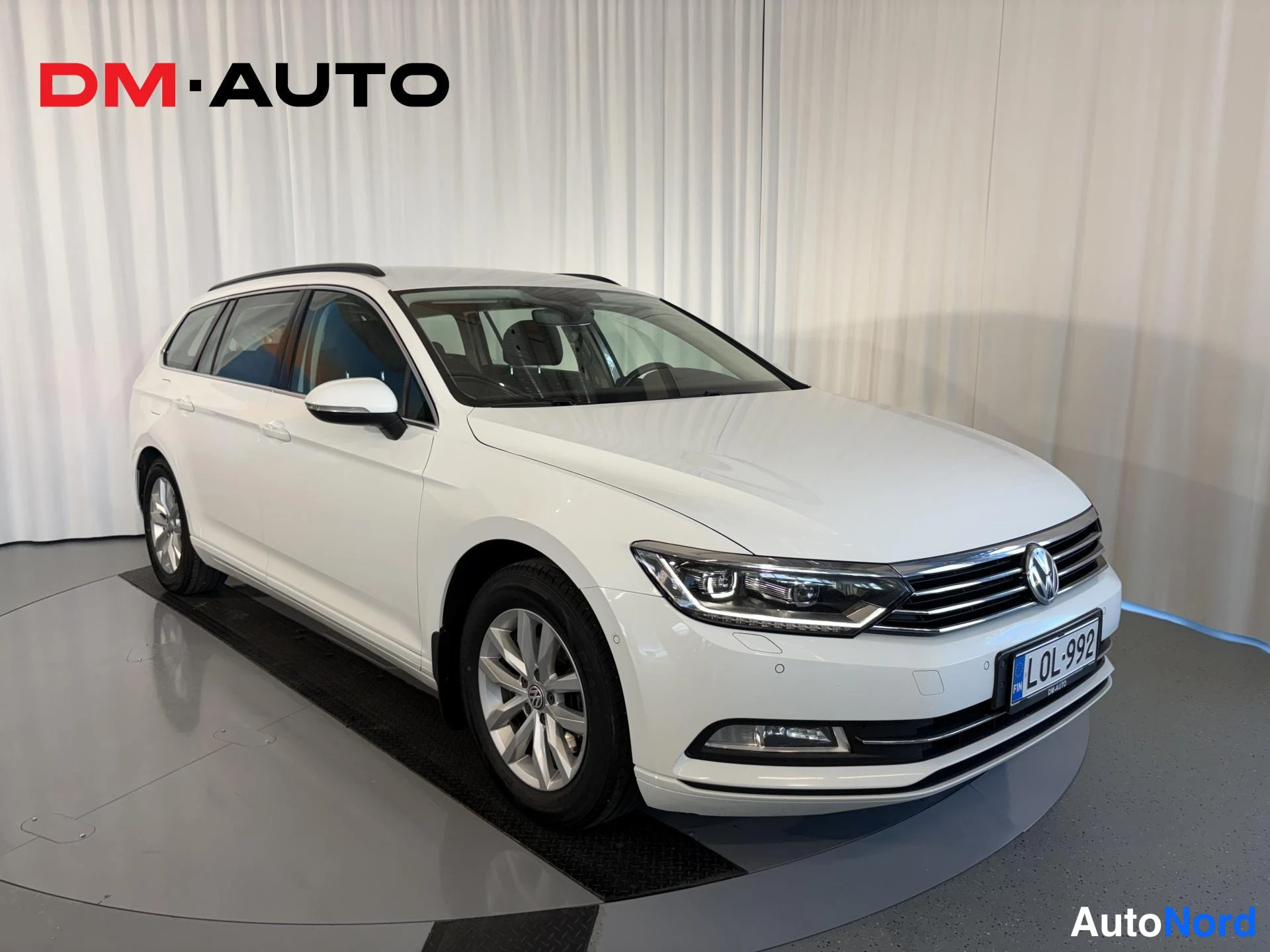 Etuviisto, nokka oikealle: Valkoinen Volkswagen Passat Variant kolmannespuolelta edestä, kylki ja etupuoli näkyvissä, rekisterikilpi, kattokaiteet havaittavissa.