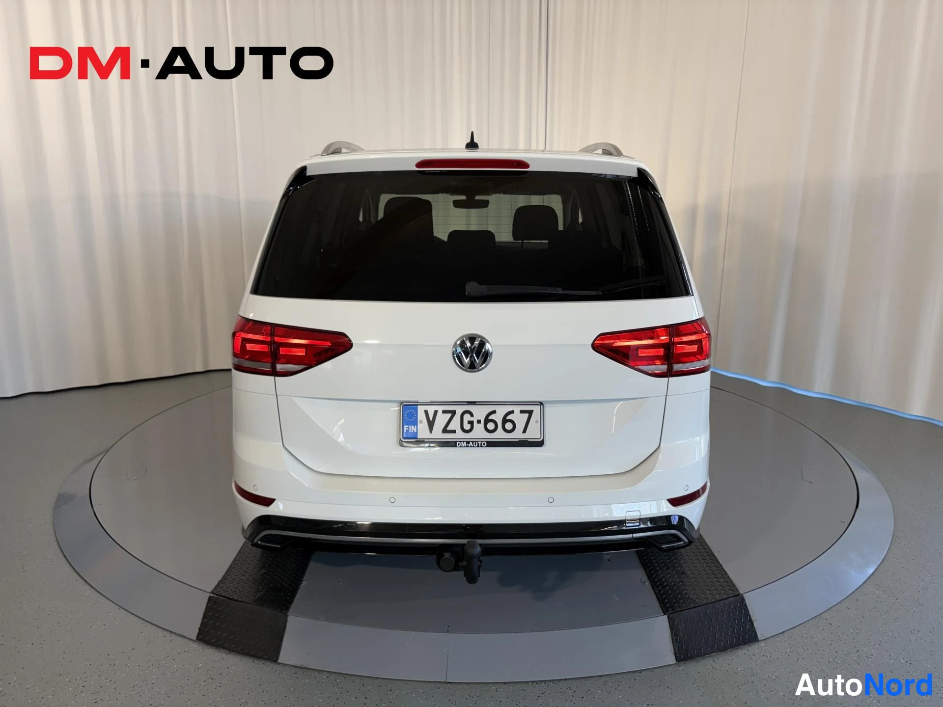 Takaa: Volkswagen Touran, takaa kuvattu valkoinen farmariauto; näkyvissä takavalot, VW-merkki, rekisterikilpi, takavilkkuja ja koukku takapuskurin alla.