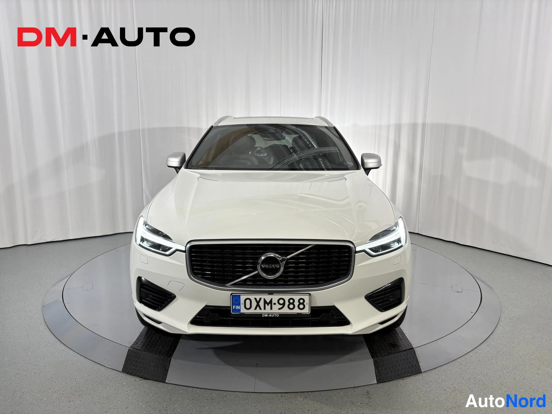 Edestä: Valkoinen henkilöauto suoraan edestäpäin, rekisterikilpi ja VOLVO-merkki etusäleikössä.