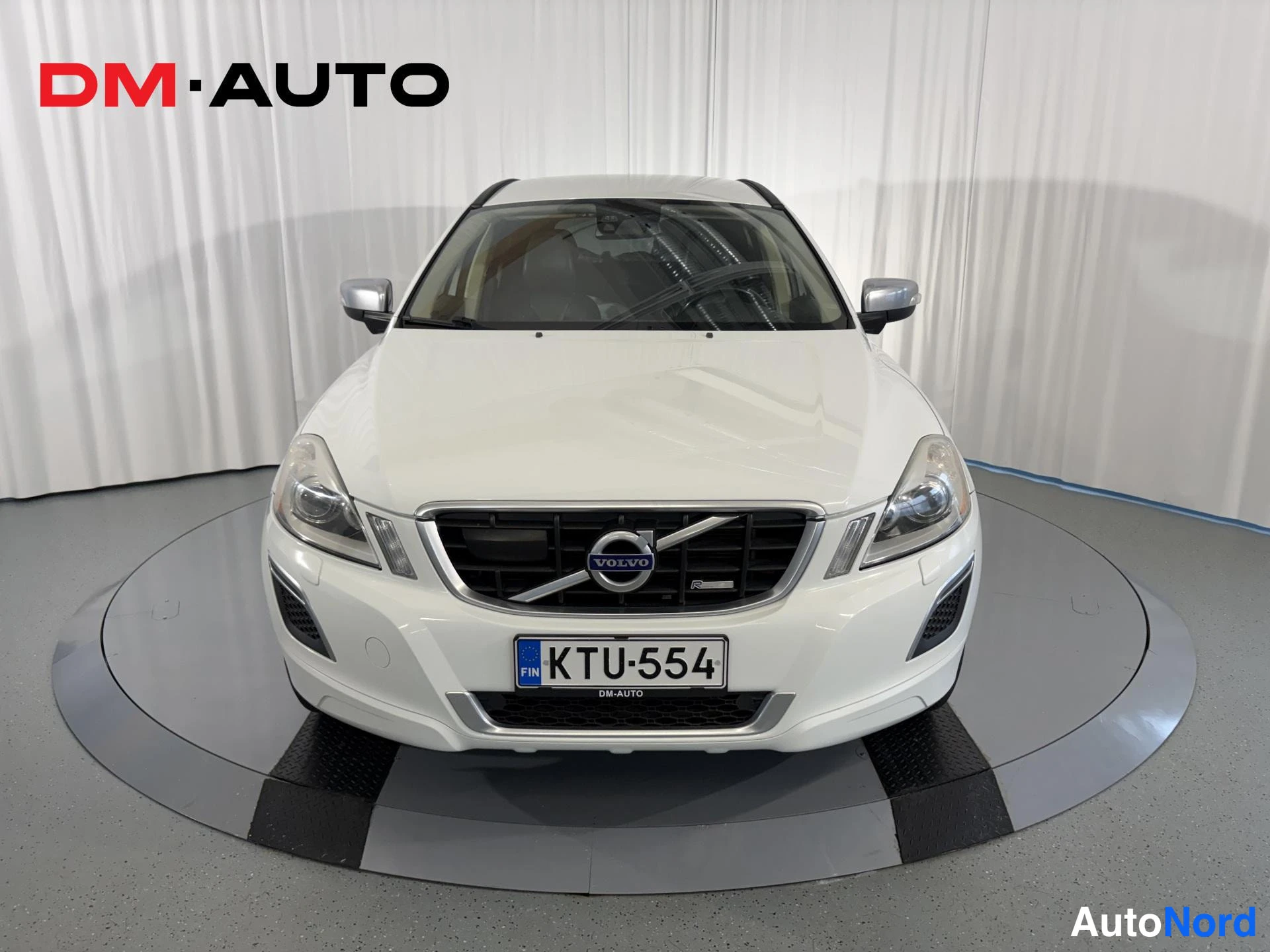 Edestä: Valkoinen Volvo XC60 suoraan edestä, VOLVO-merkitty etusäleikkö ja rekisteritunnus näkyvät.