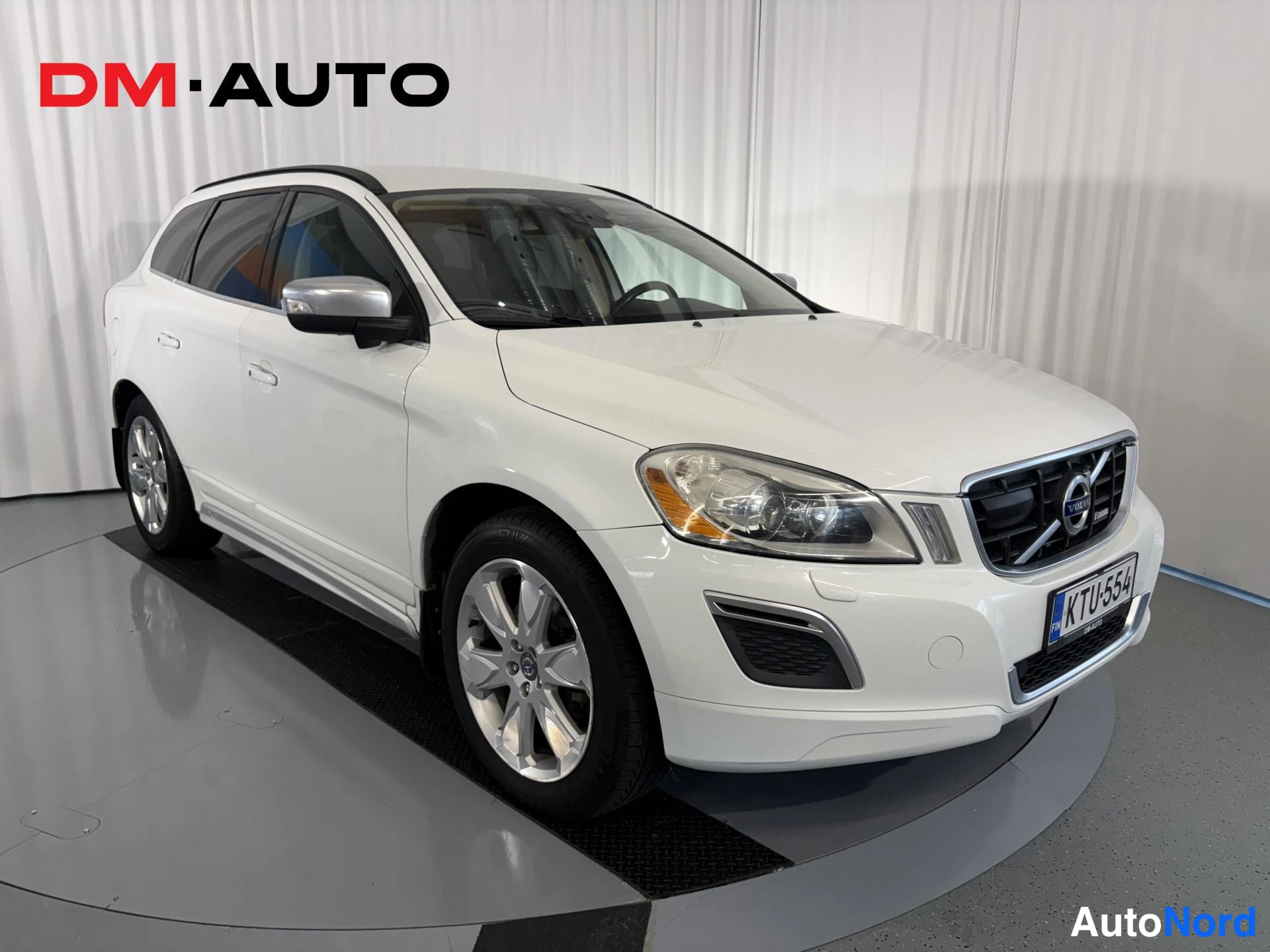 Etuviisto, nokka oikealle: Valkoinen Volvo XC60 etuosa kolmasosakulmasta oikealle, etusäleikkö ja sivuilmaisin näkyvät, rekisteritunnus.