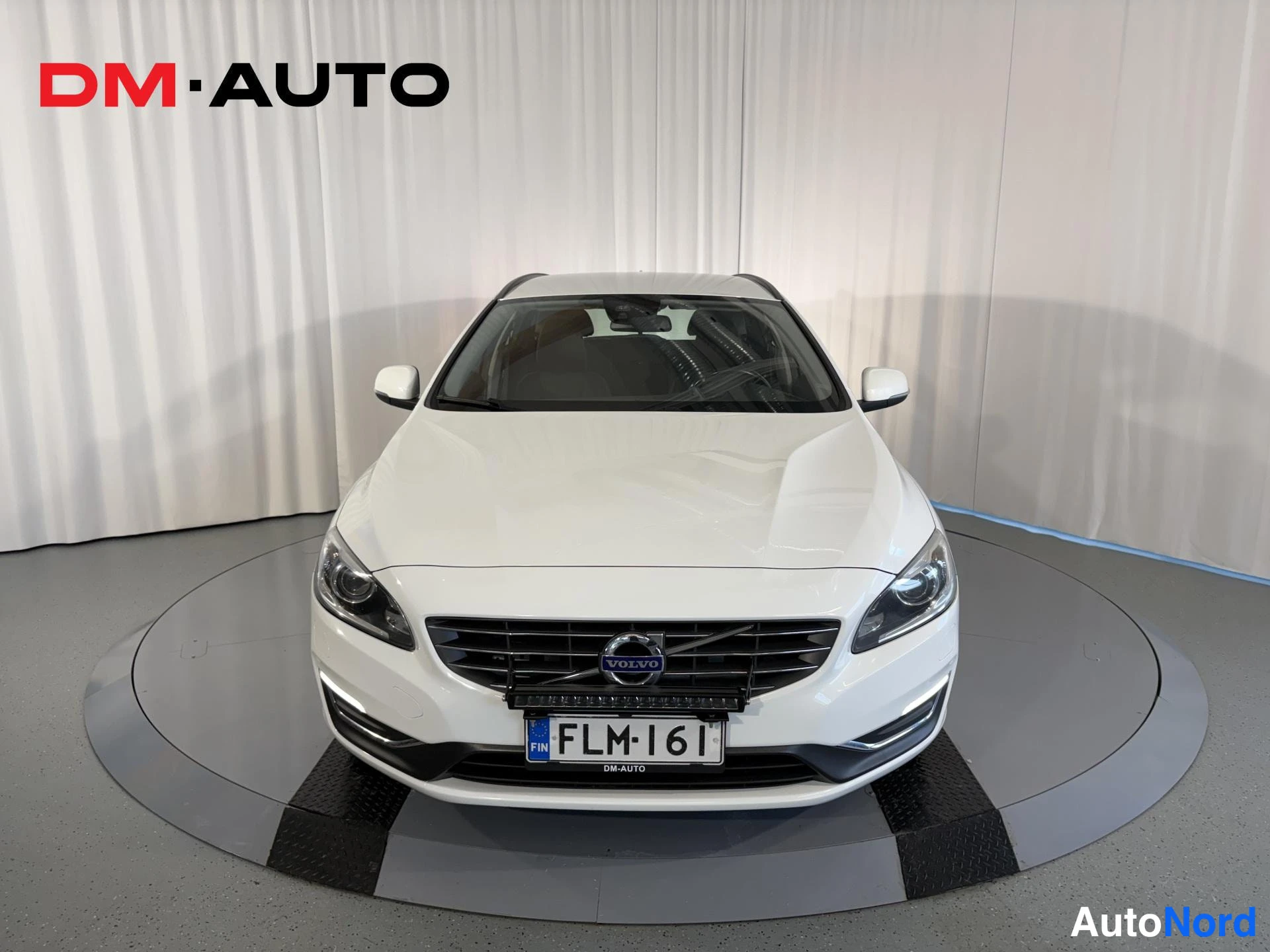 Edestä: Suora etunäkymä valkoisesta Volvo V60 -farmariautosta, etusäleikkö ja rekisterikilpi näkyvissä.