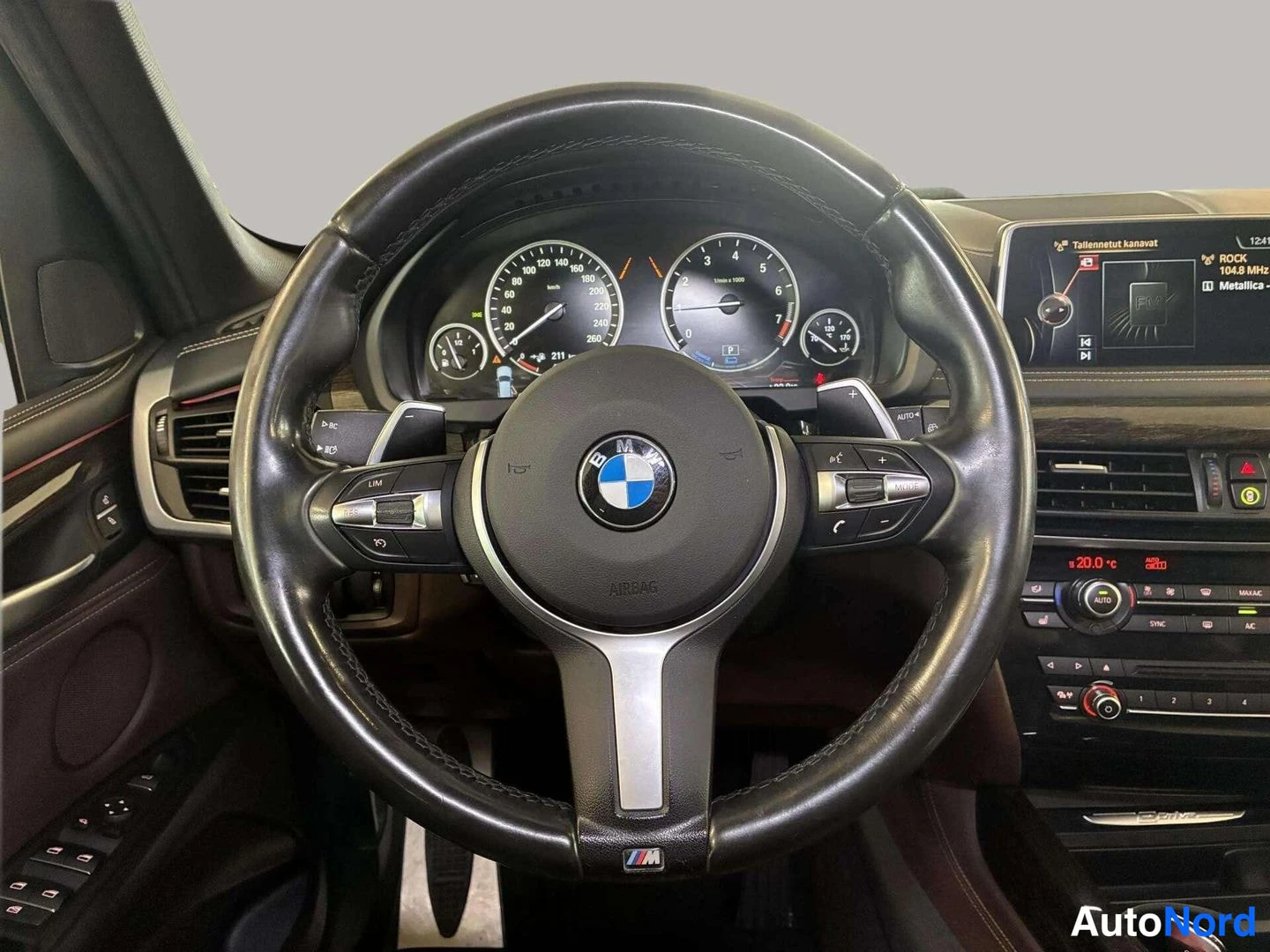 Muu: Ohjaamosta näkyy musta BMW-M-ohjauspyörä, analogiset mittarit ja keskikonsoli, jonka näytössä lukee 'Tallennetut kanavat' ja 'Metallica'.