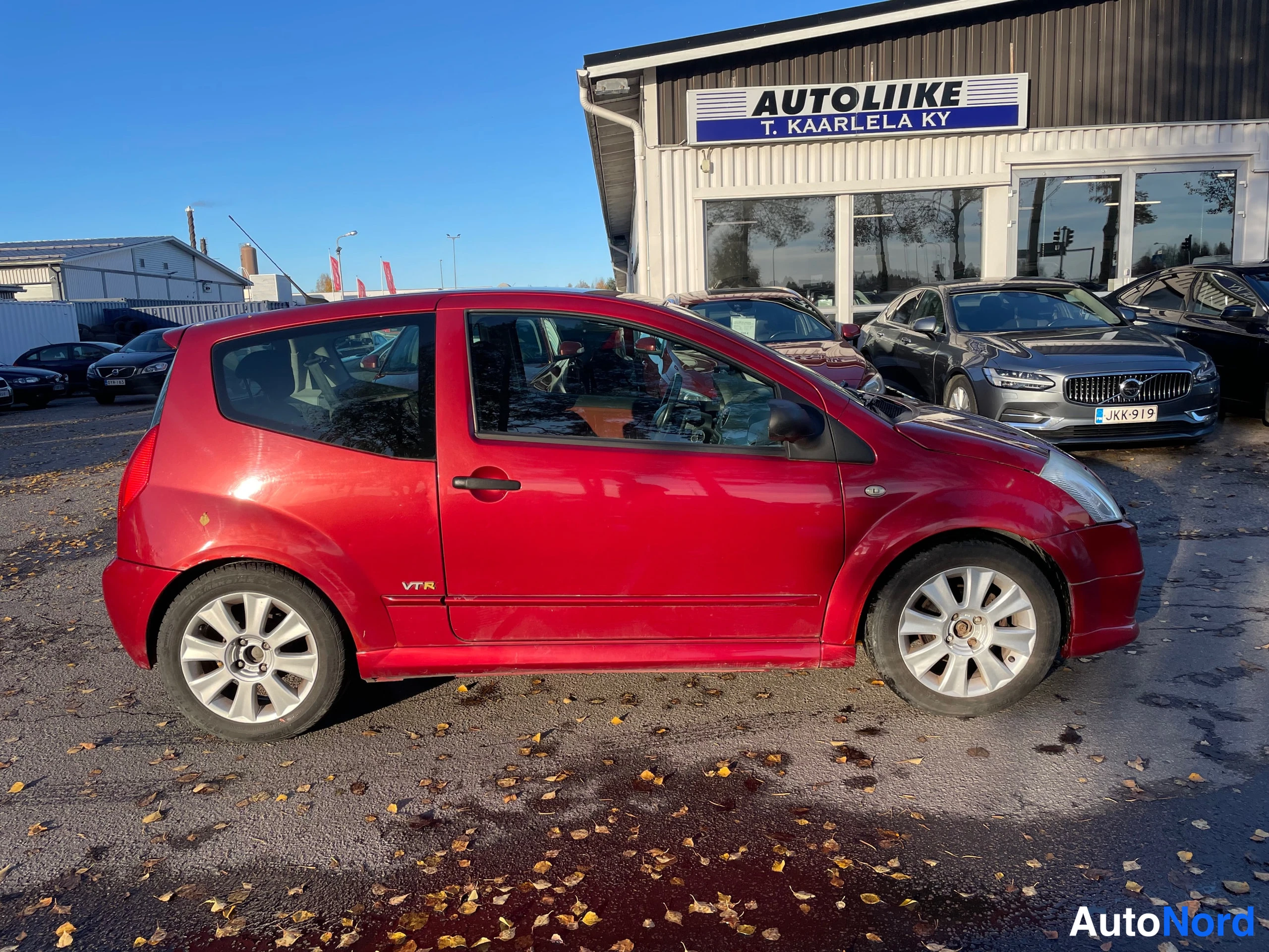 Etuviisto, nokka oikealle: Citroen C2, punainen kolmiovi hatchback, etu-kolmannes kuvassa oikealla, auton oikea kylki näkyvissä.