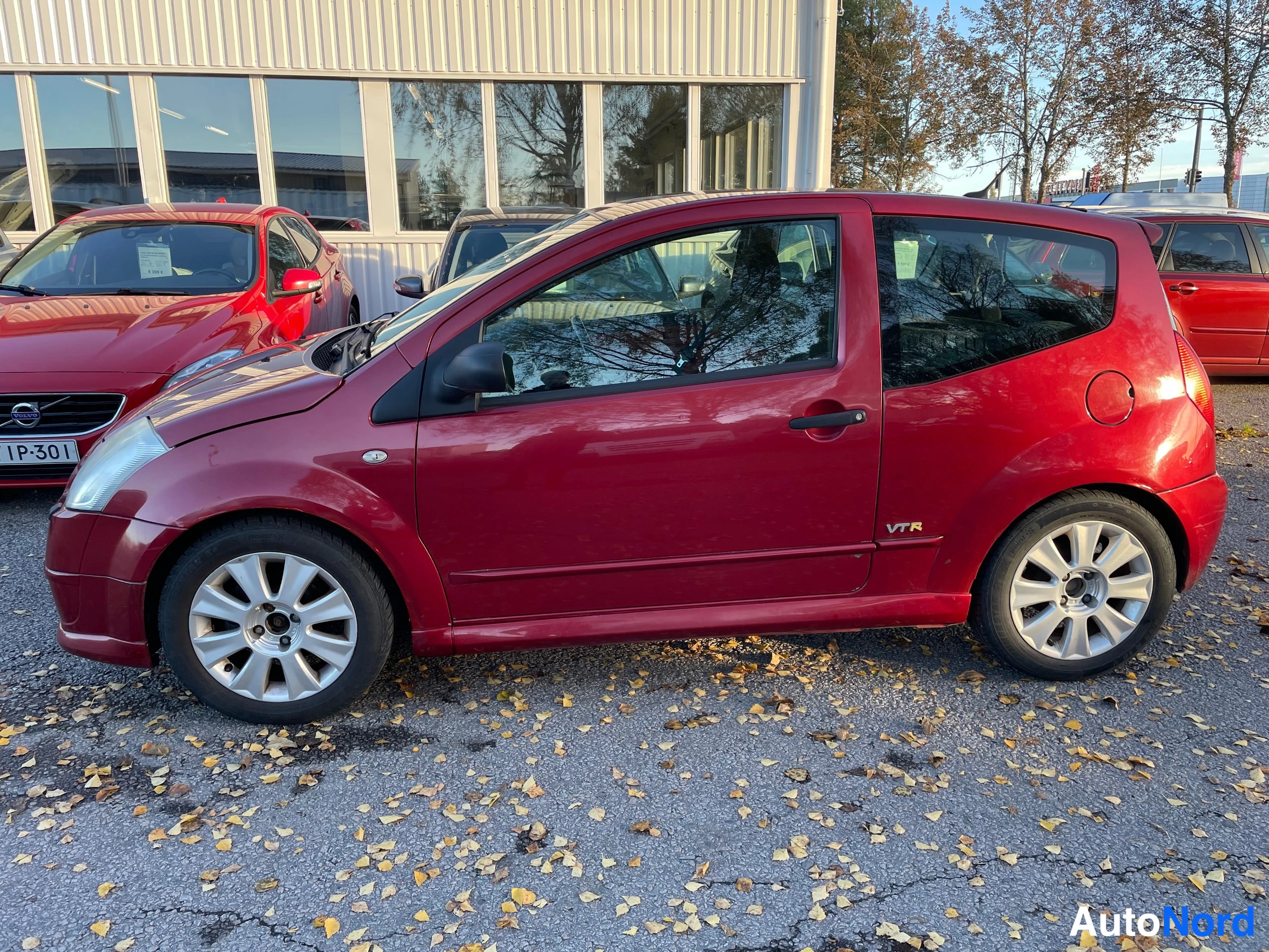 Etuviisto, nokka vasemmalle: Citroen C2, punainen kolmiovi hatchback, keula kuvassa vasemmalla, auton vasen kylki näkyvissä.