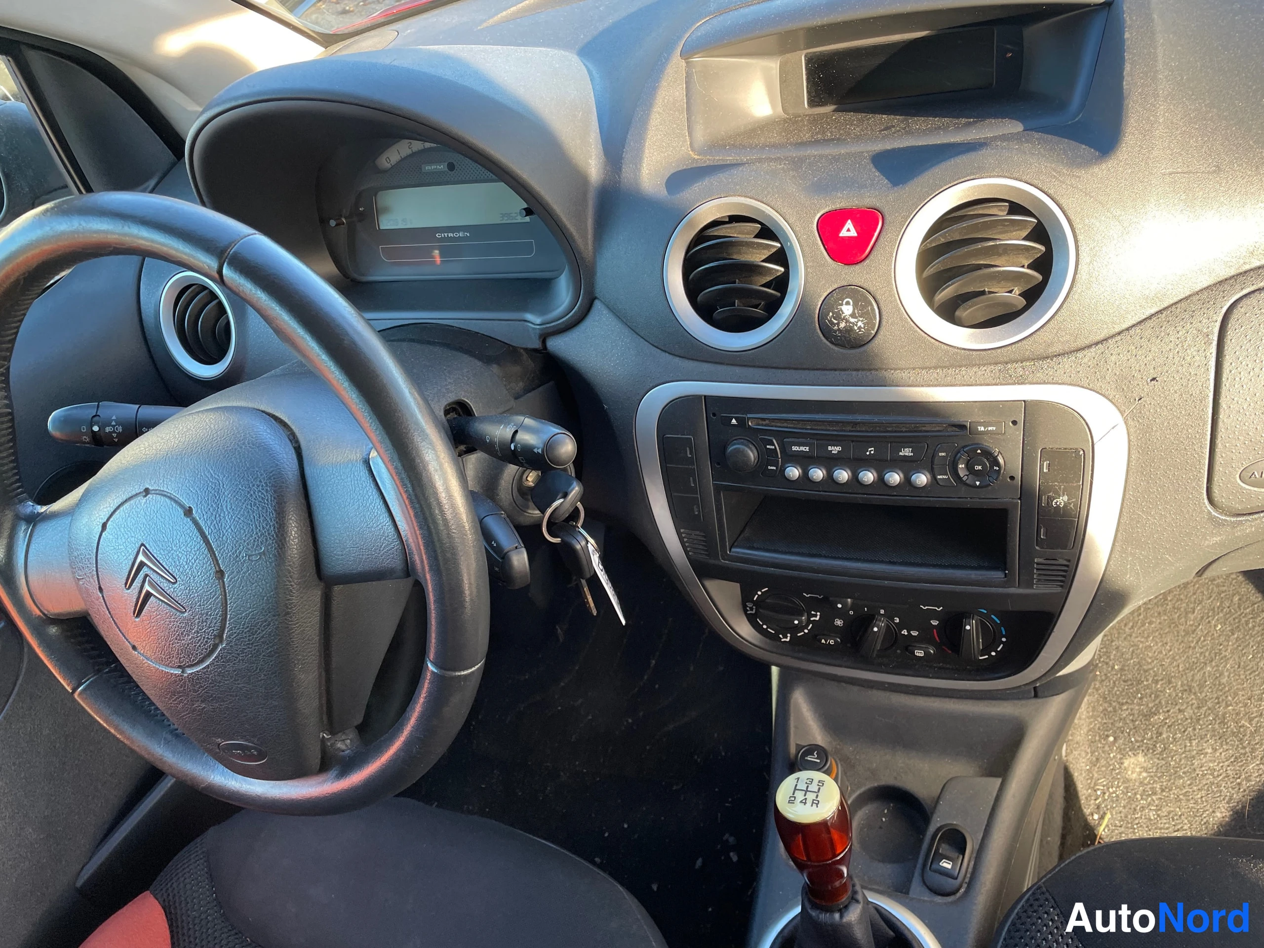 Muu: Ohjaamosta lähikuva: Citroën-ohjauspyörä, kojelauta, radio ja käsivaihtoea, jossa viisivaihteinen vaihtoehtokuvio.