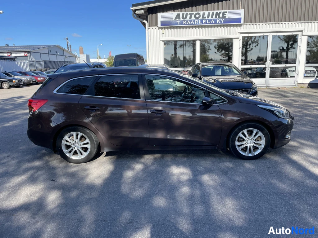 Sivulta: Kia Ceed -farmariauto sivulta kuvattuna, ruskea koriväri, hopeiset pyöränkehät, autoliikkeen piha.