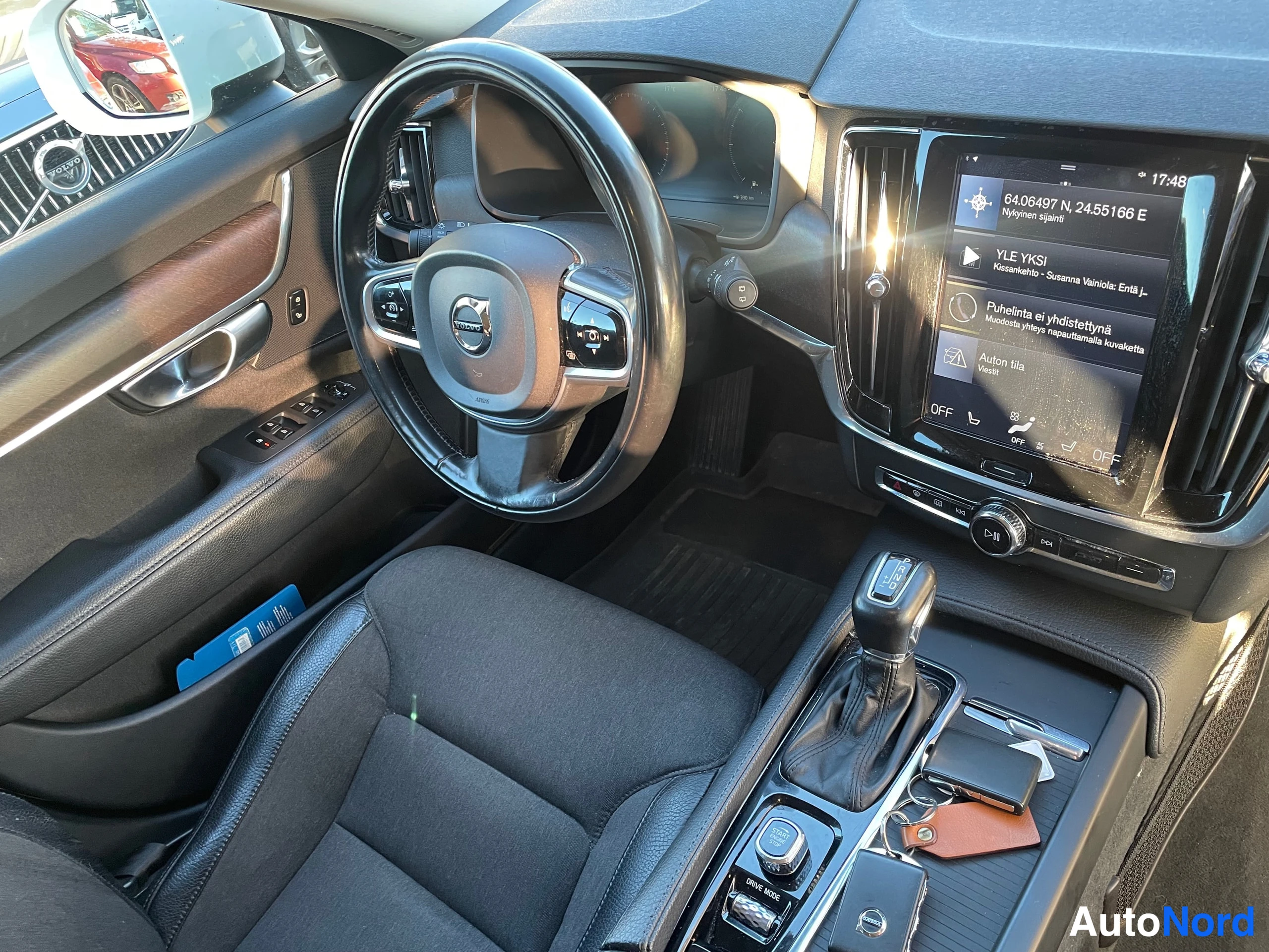 Muu: Ohjaamo kuvattuna kuljettajan puolelta: Volvo-ohjauspyörä, vaihteenvalitsin, keskinäyttö ja auton avaimet konsolilla.
