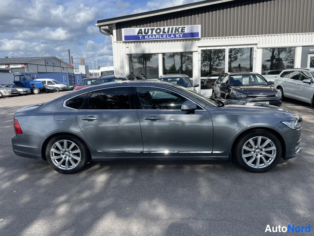 Sivulta: Harmaan Volvo S90 -sedanin vasen kylki täydessä sivuprofiilissa autoliikkeen edessä.