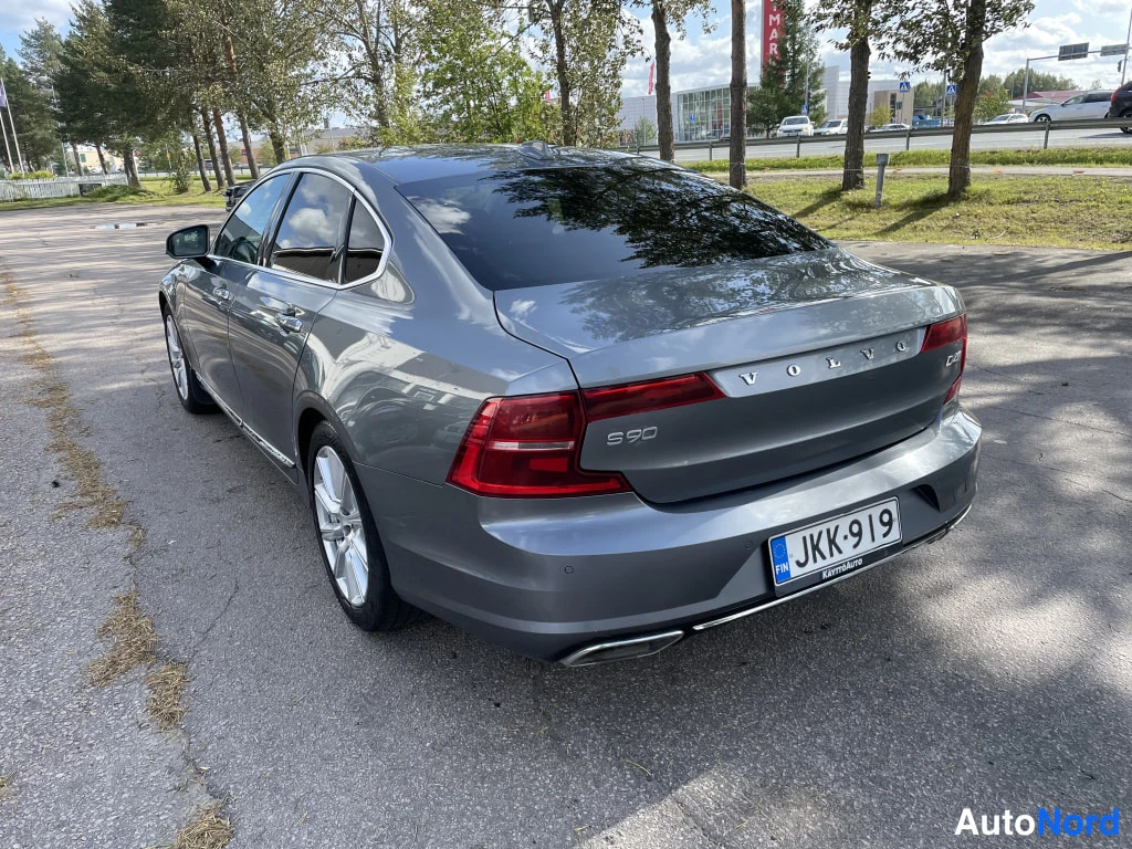 Takaviisto: Harmaan Volvo S90 -sedanin takakulma tieltä katsottuna, S90-merkintä ja rekisteritunnus näkyvissä.