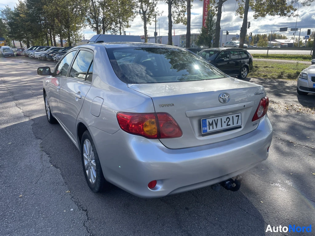 Takaviisto: Toyota Corolla -sedan takaokolikuva vasemmalta, takavilkku ja valjaskoukun pallo näkyvissä, rekisteritunnus.