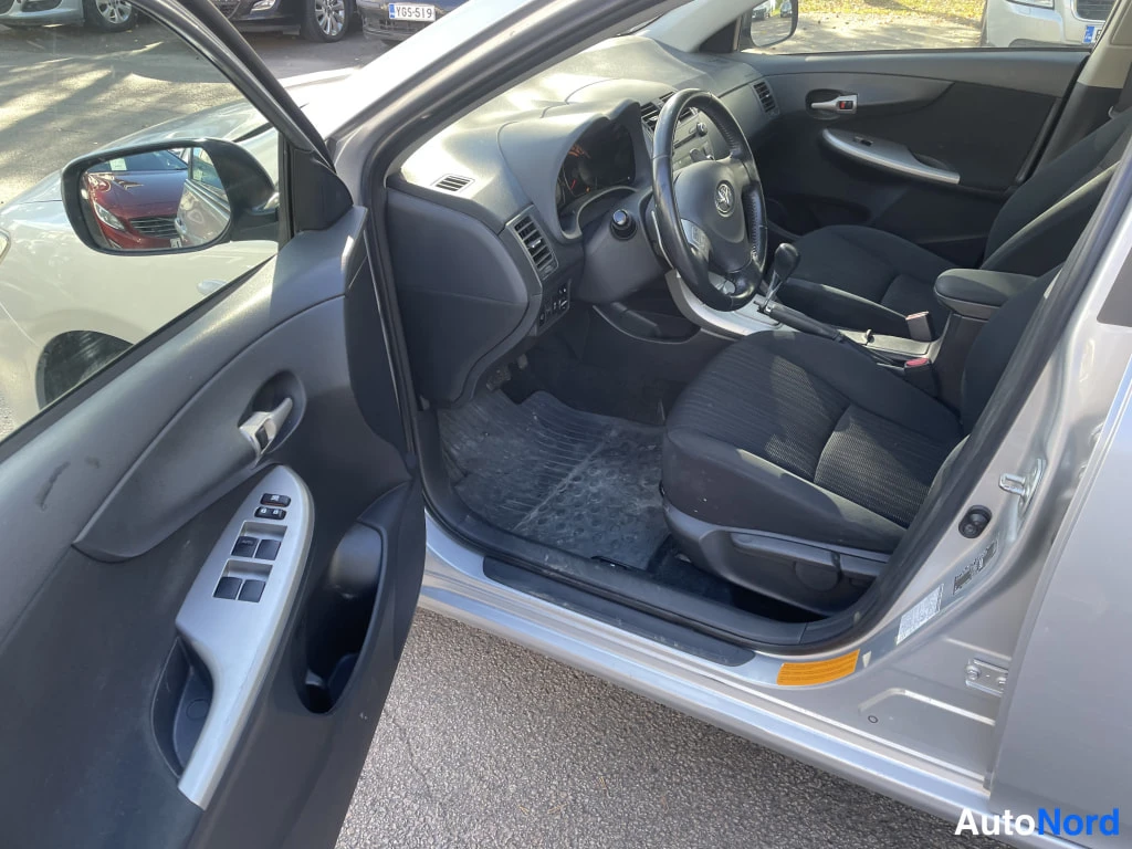 Muu: Avoimesta etuovesta näkyy Toyota Corollan etumattomat istuimet, ohjaamo ja oven ikkunoiden kytkimet.