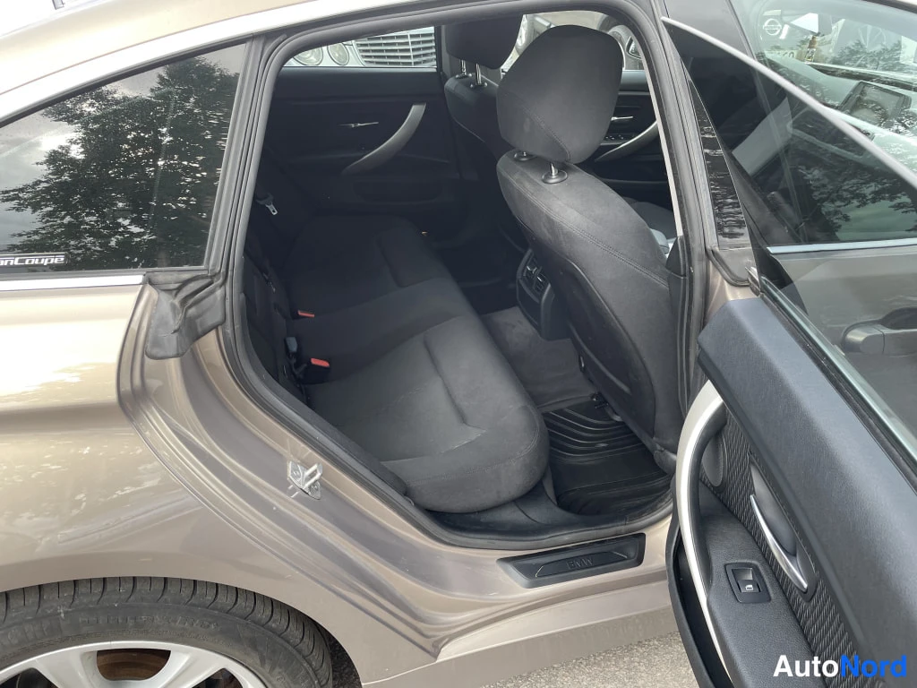 Sivulta: Avoimesta takavästystä näkyy BMW:n takapenkkien tummat kangasistuimet ja tumma matto; korirakenne on beige-harmaa.
