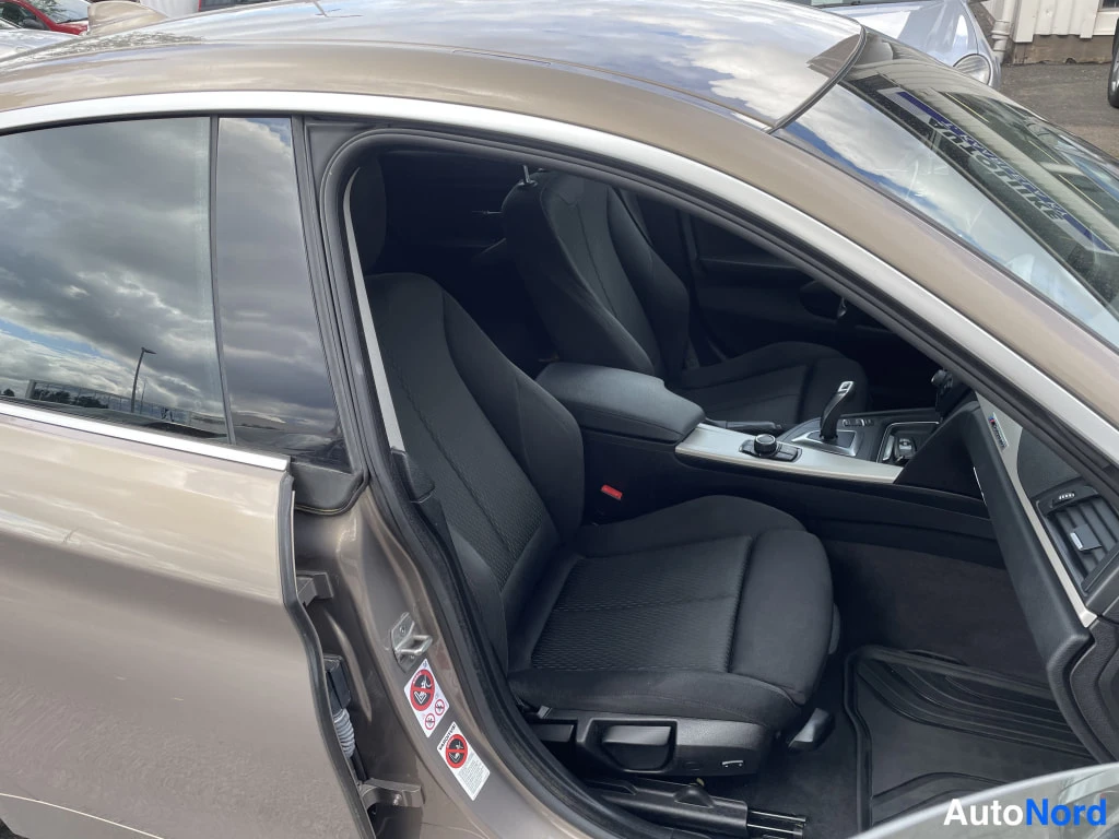 Sivulta: Avoimen etuoven kautta näkyvä BMW:n etupenkki, tummat kangasistuimet ja keskikonsolin vaihteenvalitsin.