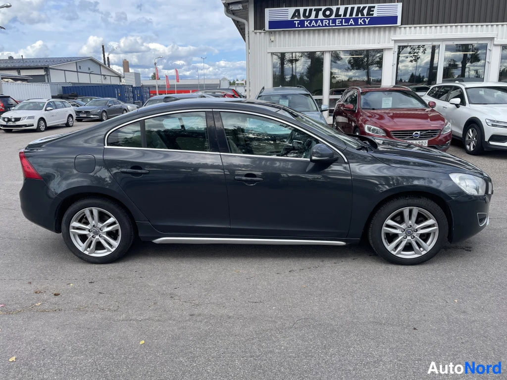 Sivulta: Tummanharmaan Volvo S60 -henkilöauton vasen kylki kuvattu sivulta autotallin pihalla.