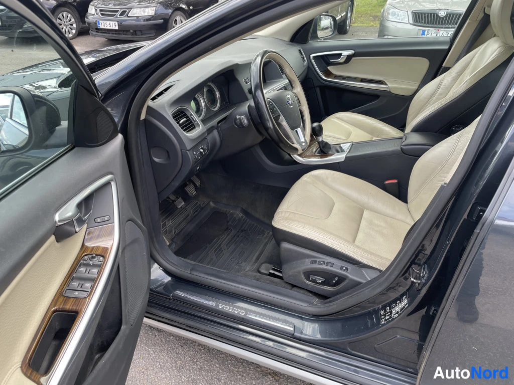 Sivulta: Avatun etuoven sisäpuoli: beige nahkaverhoilu, ohjauspyörä ja tumma kojelauta; kynnyksellä VOLVO-teksti.