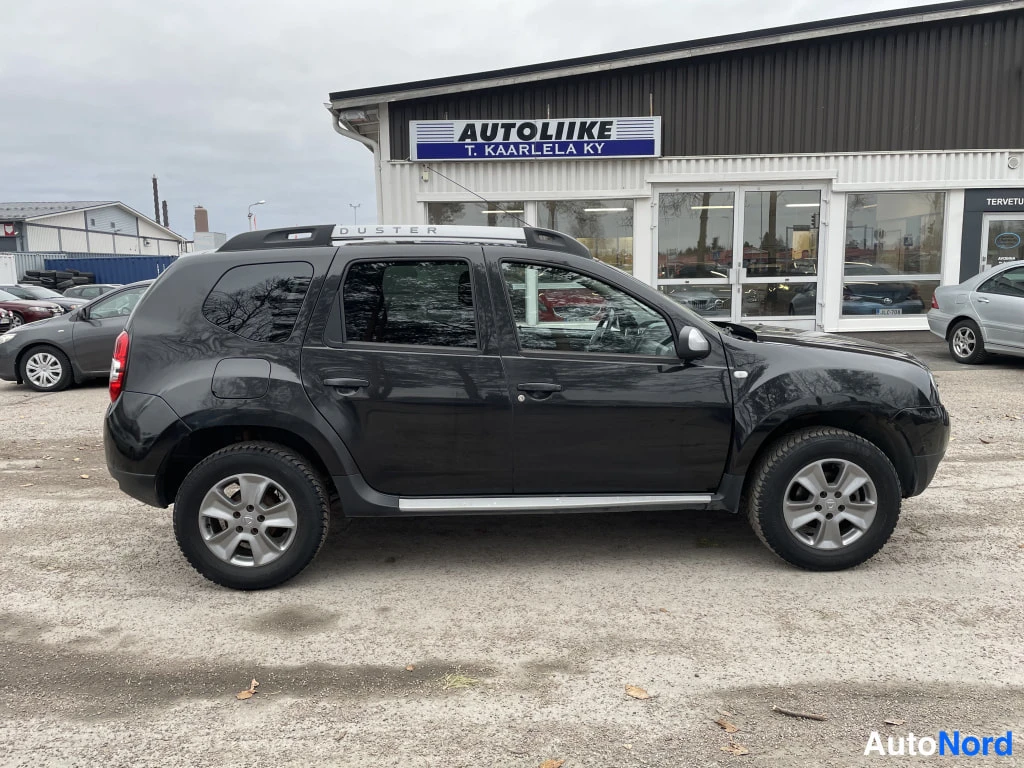 Sivulta: Musta Dacia Duster sivulta oikealta kattokaiteilla ja ovenkynsisilla listoilta.