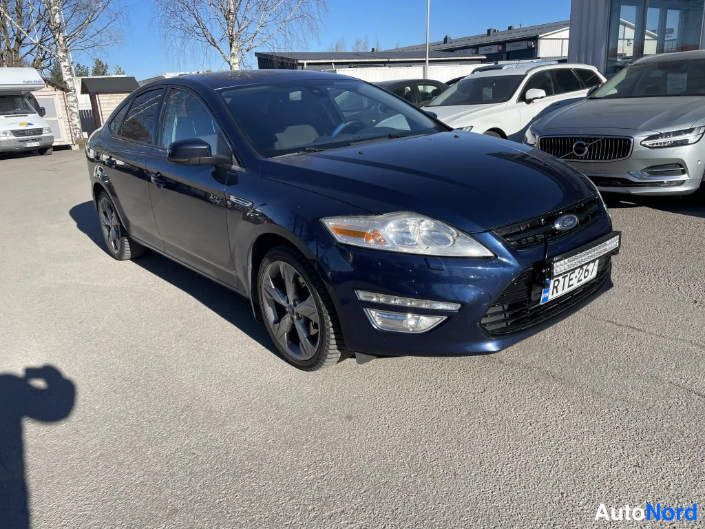 Etuviisto, nokka oikealle: Tummansininen Ford Mondeo -sedan kulmassa edestä oikealta, etusäleikkö ja ajovalot näkyvät.