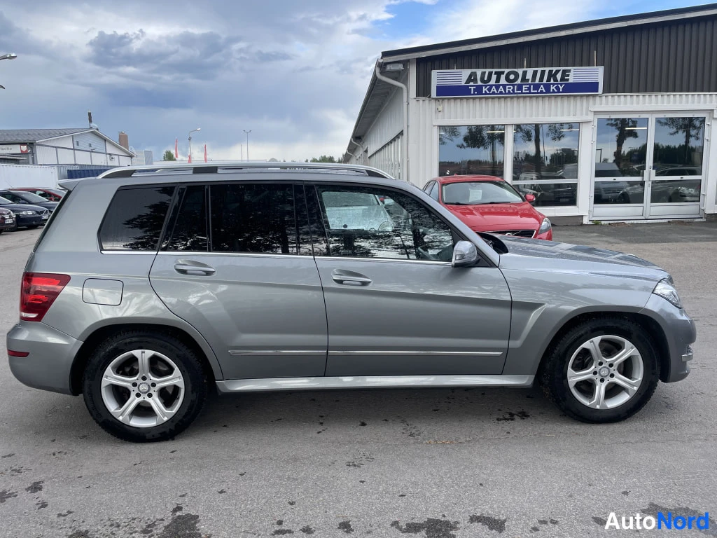 Sivulta: Mercedes-Benz GLK sivuprofiilista, molemmat sivut ja kattokaiteet näkyvät, taustalla Autoliike T. Kaarlela Ky -rakennus.