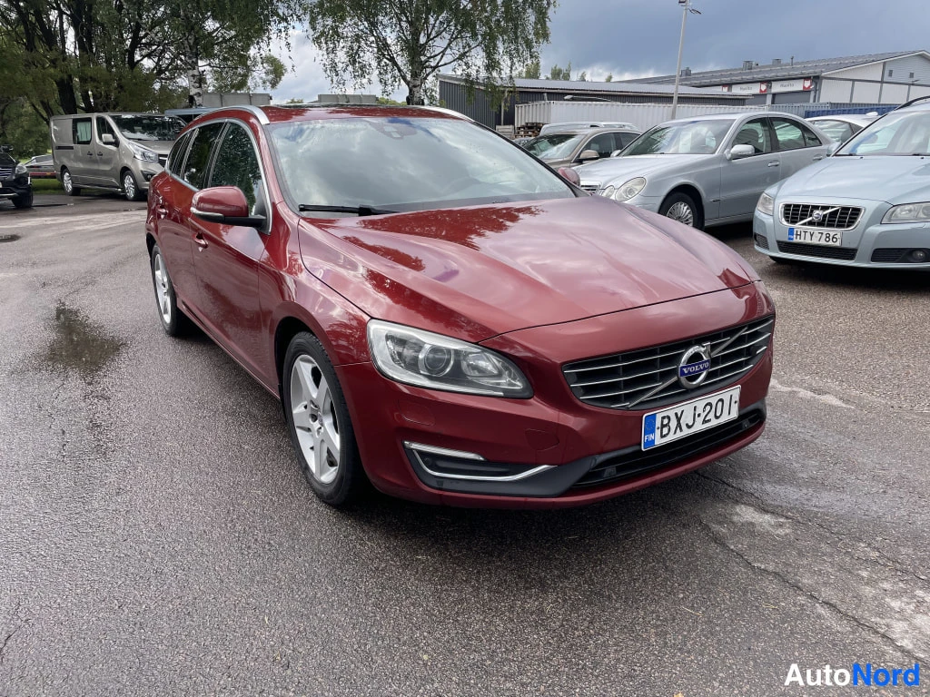 Etuviisto, nokka oikealle: Punainen farmariauto kolmanneltpä edestä vasemmalle kuvattuna, rekisterikilpi, Volvo-merkki etusäleikössä.