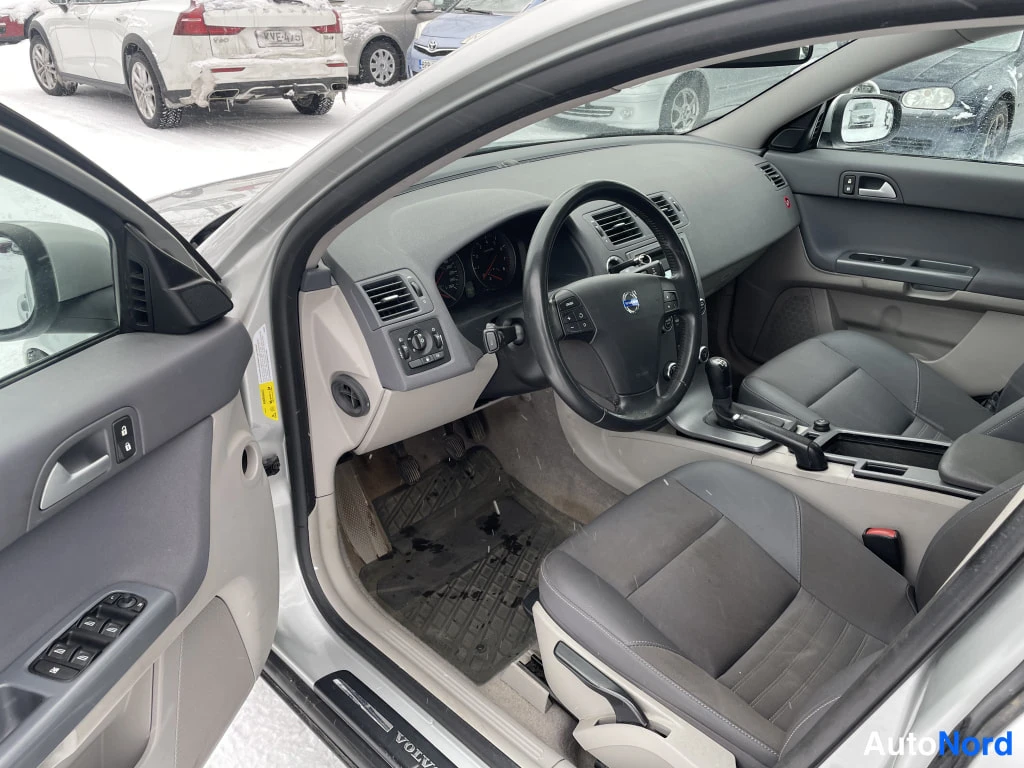 Muu: Autojen ohjaamo vasemmalta oven auki: harmaa kojelauta, Volvo-ohjauspyörä, automaattivaihteen valitsin ja tummat etuistuimet; lattiamatot märät ja likaiset