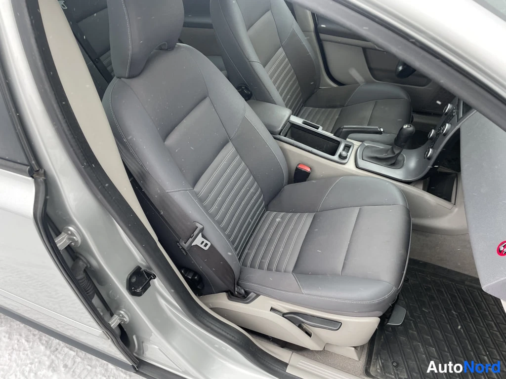 Sivulta: Kuljettajan istuin ja keskikonsoli; vaihtoehto käsivaihteen ympärillä, harmaa verhoilu ja musta kumimatka.