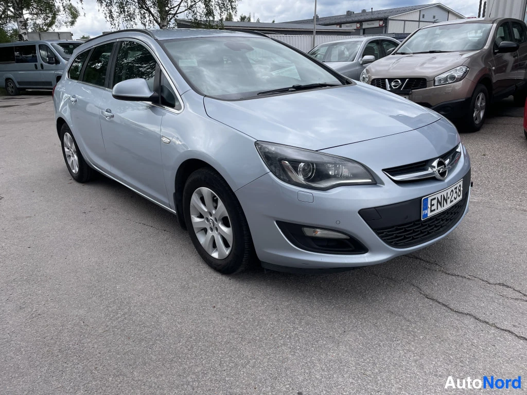 Etuviisto, nokka oikealle: Opel Astra -farmarivaaleansinisenä etukulmasta oikealta, rekisteritunnus.