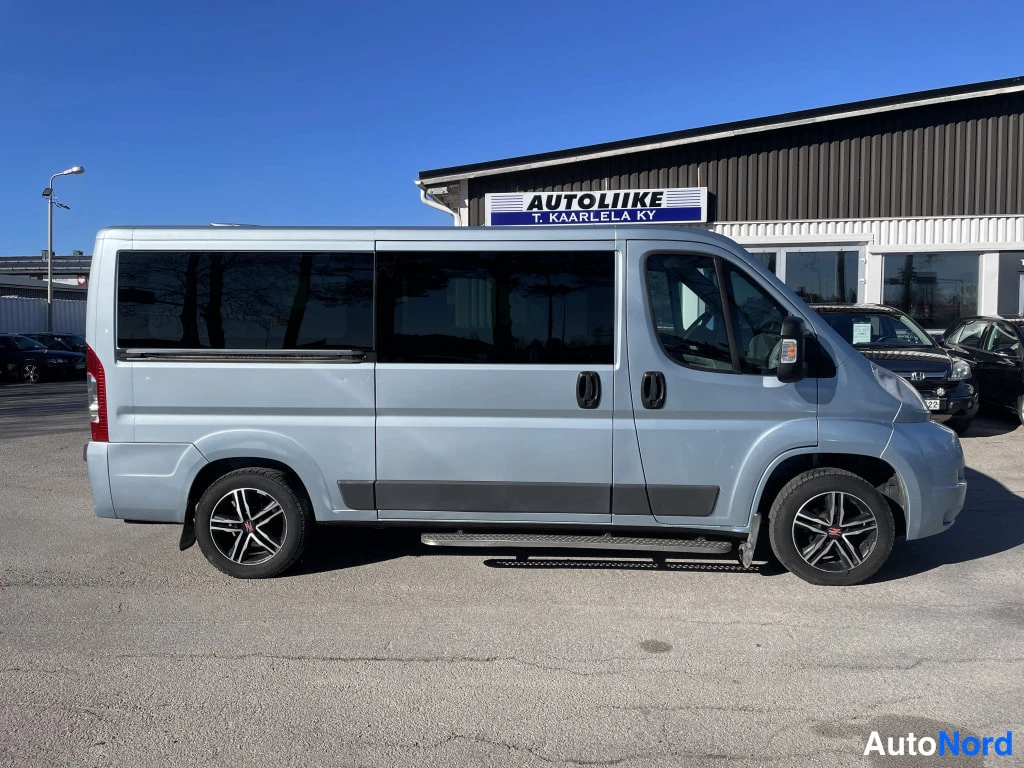 Etuviisto, nokka oikealle: Peugeot Boxer -pakettiauto sivulta, kuljettajan puoleinen kylki ja tummat ikkunat, taustalla Autoliike T. Kaarlela Ky -rakennus.