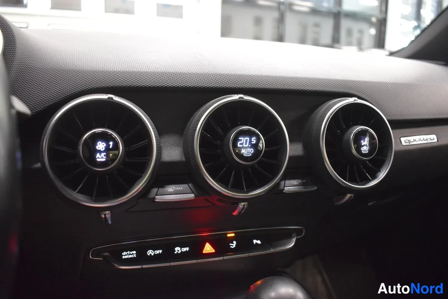 Yksityiskohta: Kojelaudan keskiosan kuva kolmella pyöreällä ilmastointiventtiilillä, keskellä näyttö jossa lukee 20.5 ja AUTO, alla rivissä napit drive select, OFF, OFF, varoi