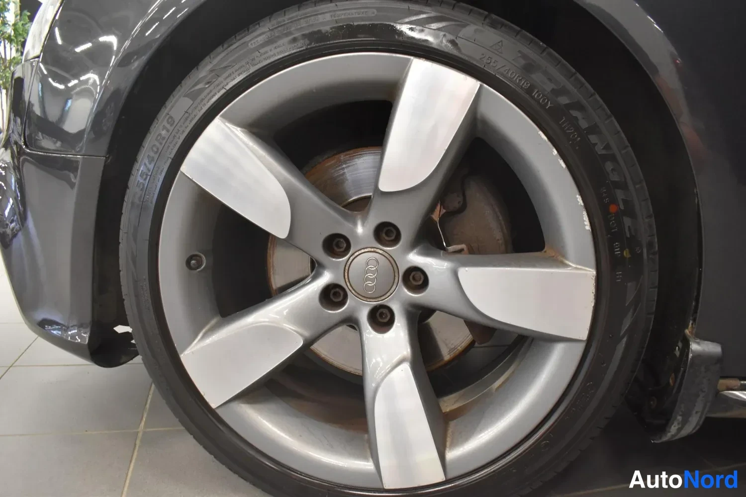 Yksityiskohta: Lähikuva auton etupyörästä: hopeaviitteinen Audi-vanne, rengas merkintä 255/40 R19, jarrulevy ja ohjaustangon nivel näkyvät.
