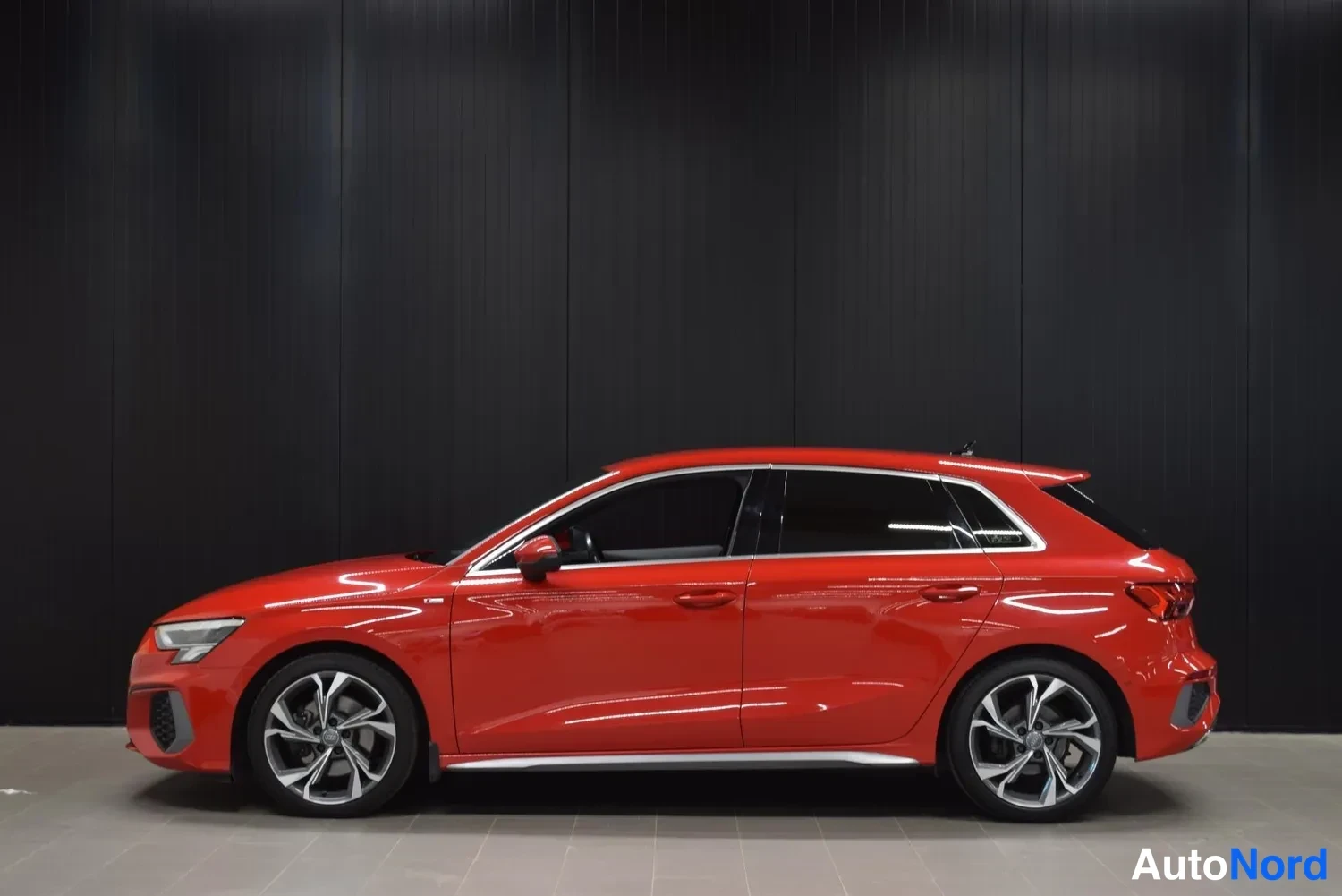 Sivulta: Punaisen Audin A3 Sportback sivuprofiili sisätiloissa.