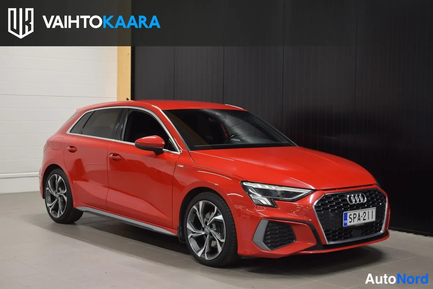 Etuviisto, nokka oikealle: Punaisen Audi A3 Sportback -auton etunurkkakuva; etusäleikö, LED-ajovalot, etupuskuri ja rekisterikilpi näkyvät.