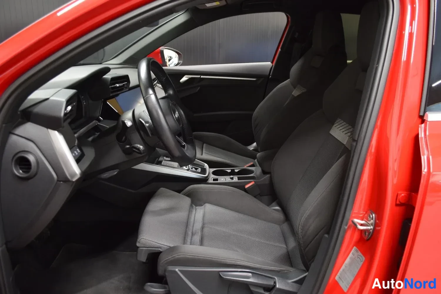 Muu: Audi A3:n sisätilat etumatkailtaaan punaisen korin välityksellä: tummat kankaanistuimet, monitoimiratti ja keskikonsoli, jonka portaali auki.