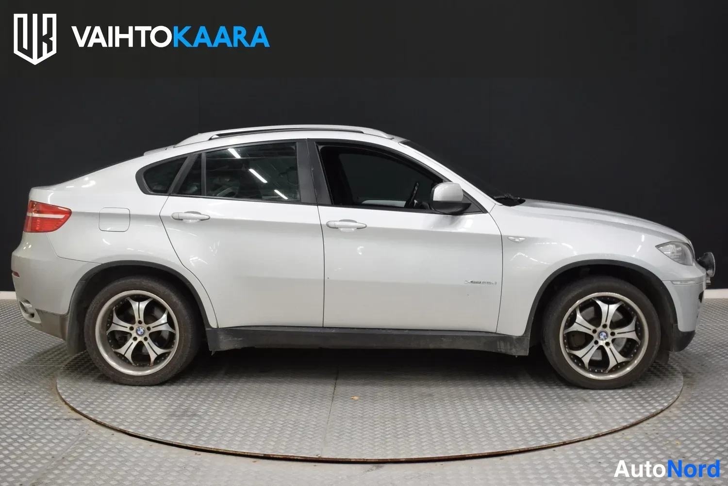 Sivulta: Sivukuva hopeanvärisestä BMW X6 -maasturista studiossa tummaa taustaa vasten.
