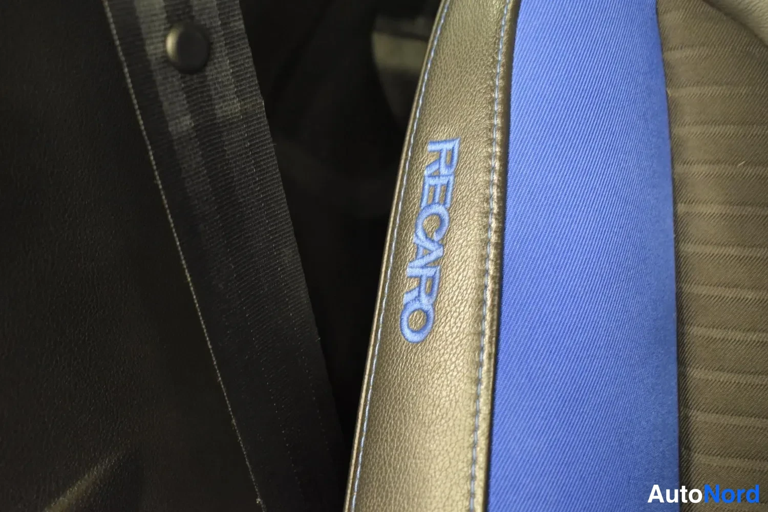 Muu: Urheiluistuimen sivupaneeli, jossa siniset RECARO-logo ja sininen kankaanosa; vieressä mustaa nahkaa ja turvavyö.