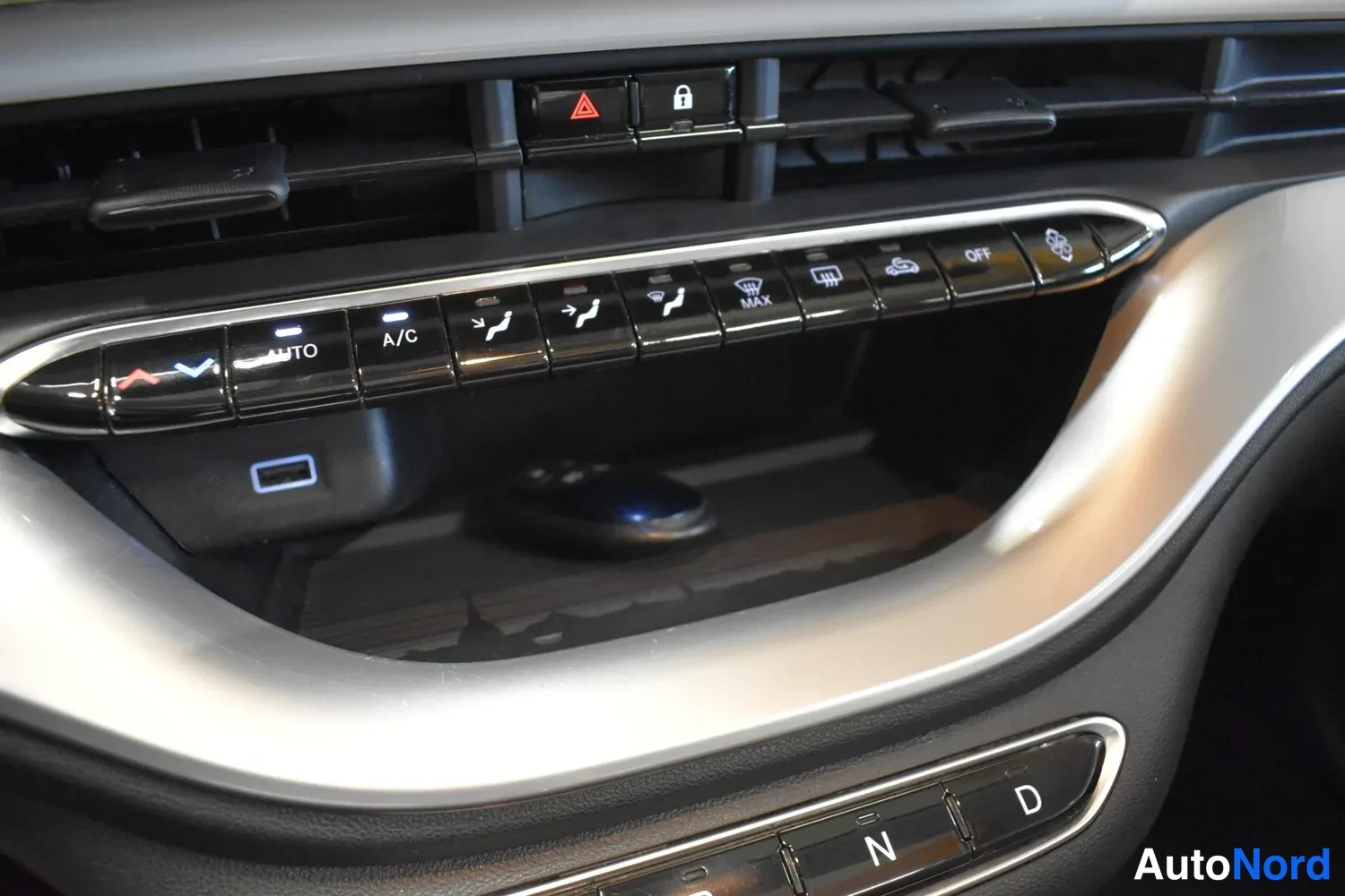 Muu: Auton kojelaudan ilmastointipaneeli, jossa AUTO-, A/C- ja MAX-painikkeet sekä sähköisen avaimen lokero.