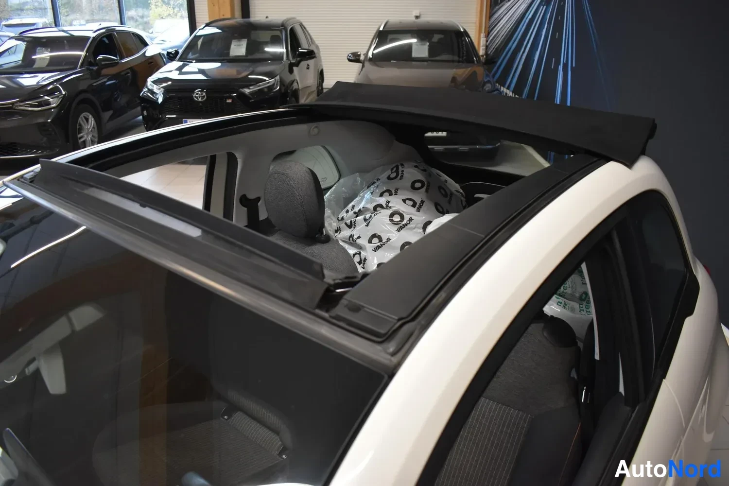 Yksityiskohta: Näkymä Fiat 500:n avoimen kankaankaton yli sisätiloihin; takapenkkiin pakkautettuja auton historia - ja varustepaketteja koskevia papereita.