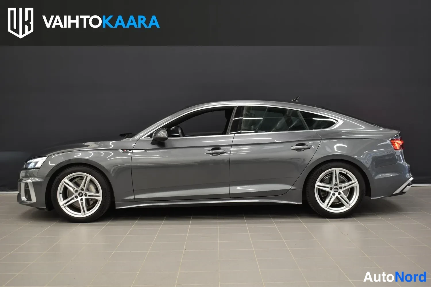 Sivulta: Audi A5 Sportback sivuprofiilista oikealta kuvattuna, tummanharmaa kori, viisitoikka-hopeavanteet.
