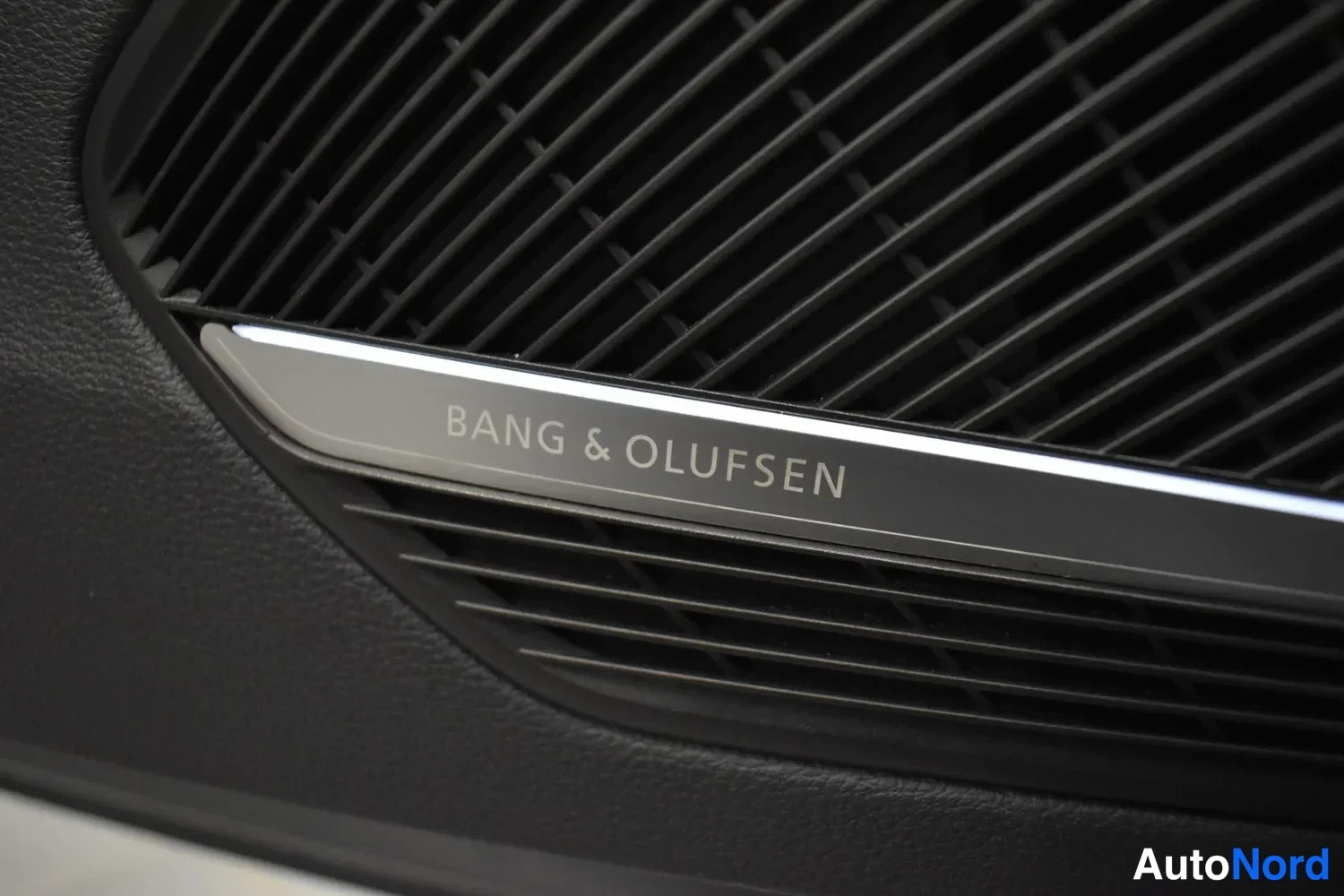 Yksityiskohta: Bang & Olufsen -kaiuttimen koriste ristikon alla tummassa sisäpaneelissa.