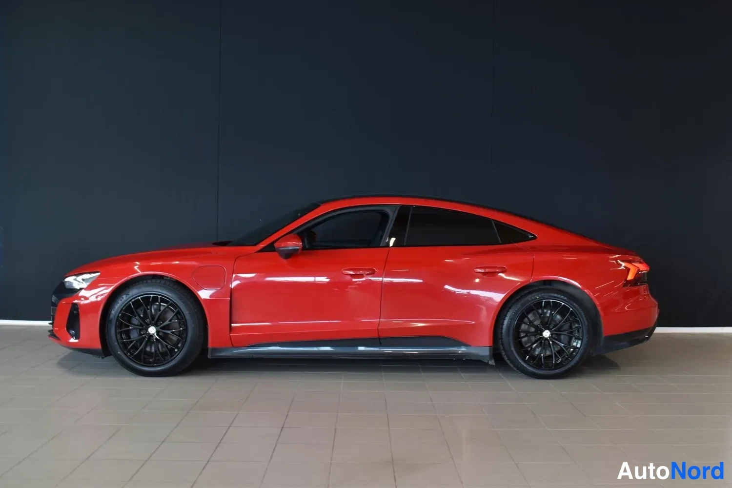 Sivulta: Punaisen Audi e-tron GT:n sivukuva sisätiloissa, mustat vanteet ja tummat ikkunat.