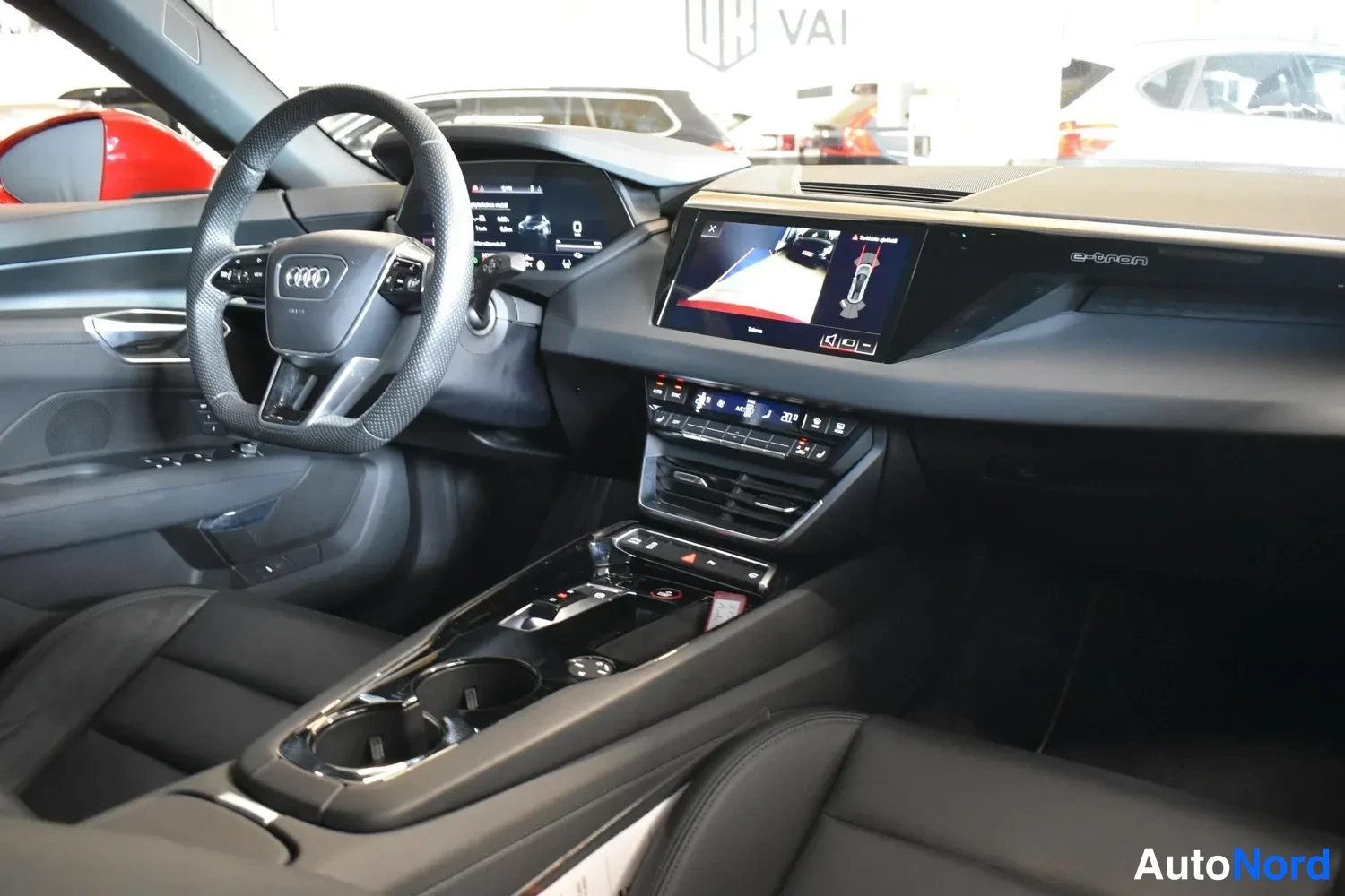 Muu: Kojelauta laajemmin: Audi-ohjauspyörä, digitaalinen mittaristo, keskusnäyttö kamera-kuvalla ja kosoliossa kortinlukijan kaltainen laite.