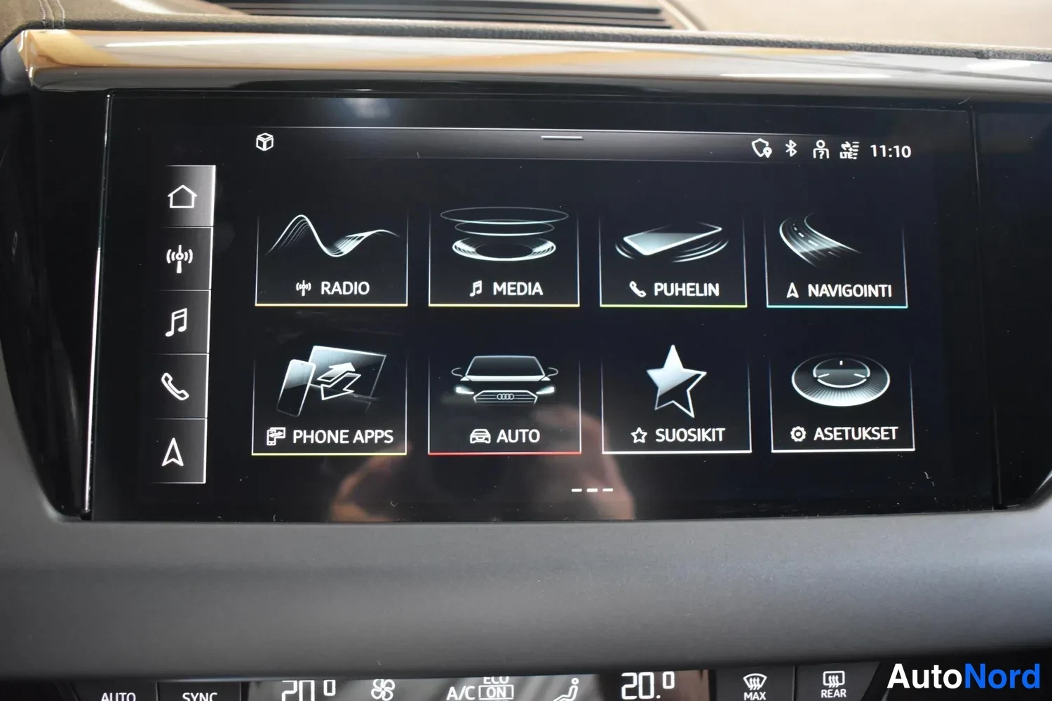 Yksityiskohta: Infotainment-järjestelmän päävalikko ruudulla: RADIO, MEDIA, PUHELIN, NAVIGOINTI, PHONE APPS, AUTO, SUOSIKIT ja ASETUKSET.