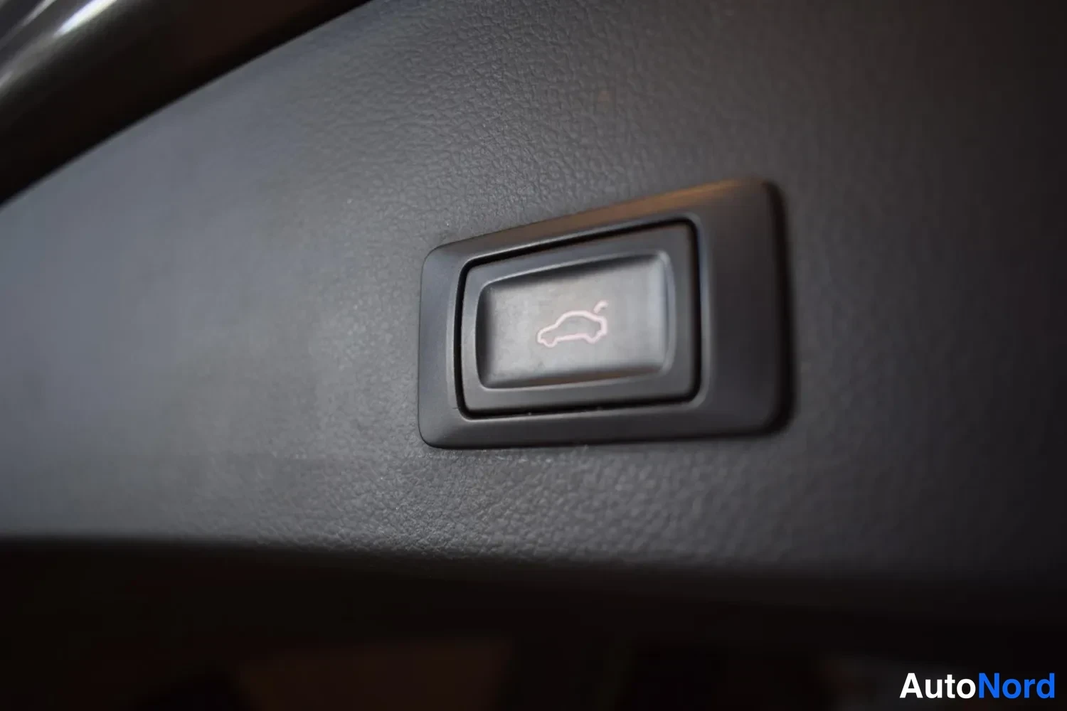 Muu: Tarkennettu kuva tummasta paneelissa olevasta nappista, jonka symbolina on auto avatulla tavaratilan kannella – tavaratilan kaukoavaus.