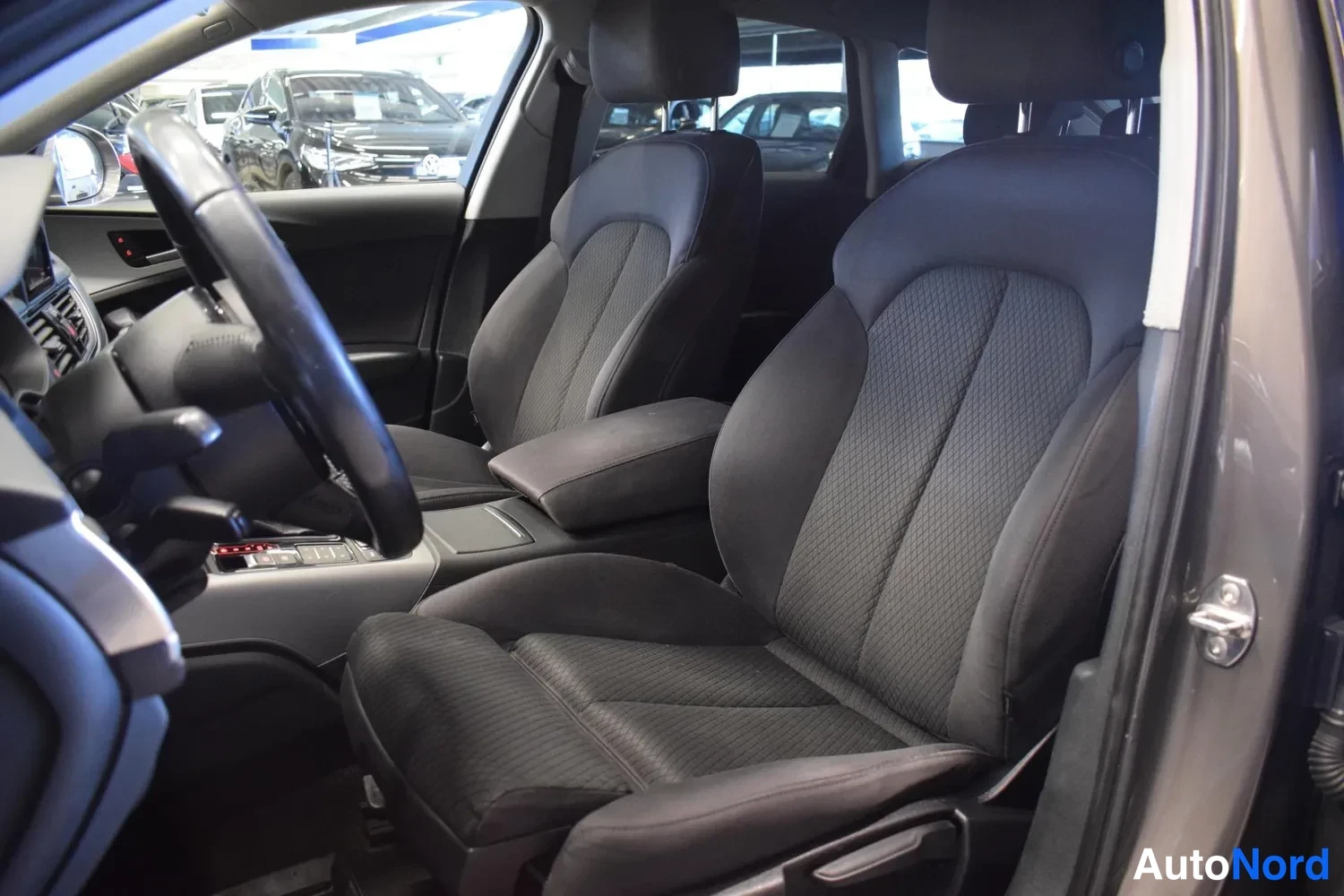 Etuistuimet: Audi A6:n etuistuimet matkumapanäkymästä: kaksi tummaa kangasistuinta ja keskikonsolilla käsinoja.