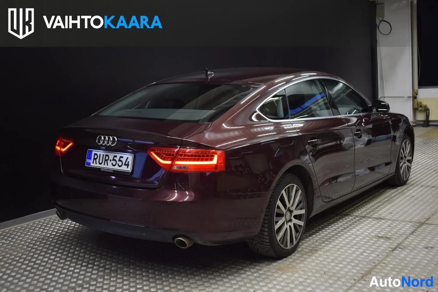 Takaviisto: Tummaviininpunaisen Audi A5 Sportbackin takanurkkakuva, takavalot ja rekisterikilpi näkyvät.