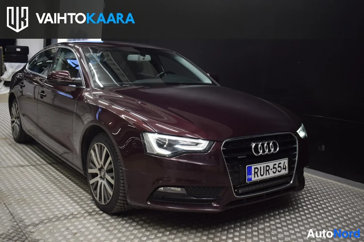 Etuviisto, nokka oikealle: Tummaviininpunaisen Audi A5 Sportbackin etunurkkakuva, etusäleikkö, LED-ajovalot ja rekisterikilpi näkyvät.