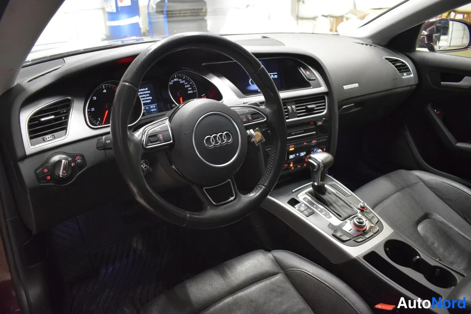 Muu: Audi A5 Sportbackin sisätilakuva: ohjauspyörä Audi-merkinnällä, kojelauta ja vaihtaja näkyvät.